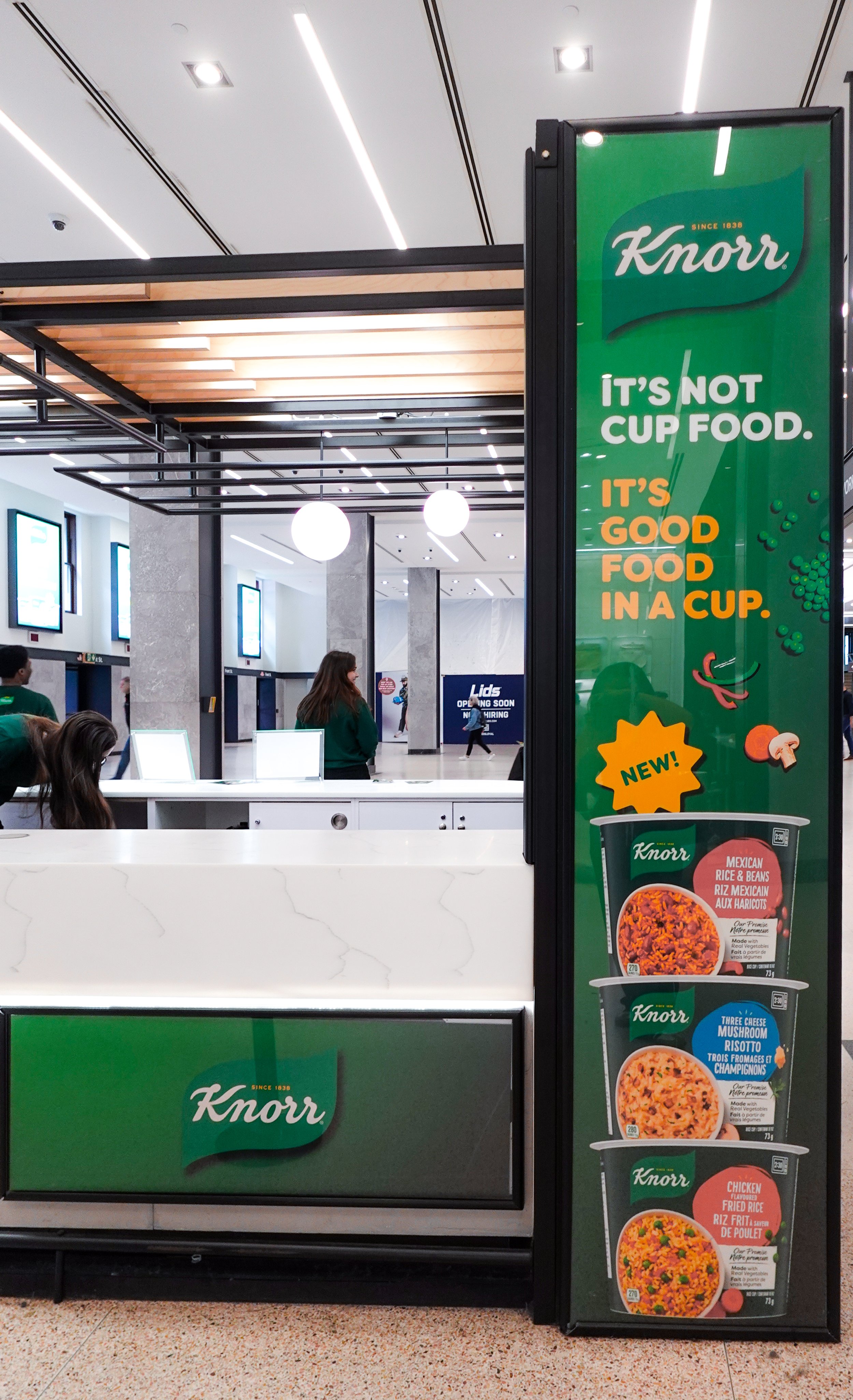 A Knorr advertisement in a grocery store featuring a slogan that says "It's not cup food, it's good food in a cup," with images of three instant rice and rice meal products displayed vertically on the right side, designed by Sunnii Studios.