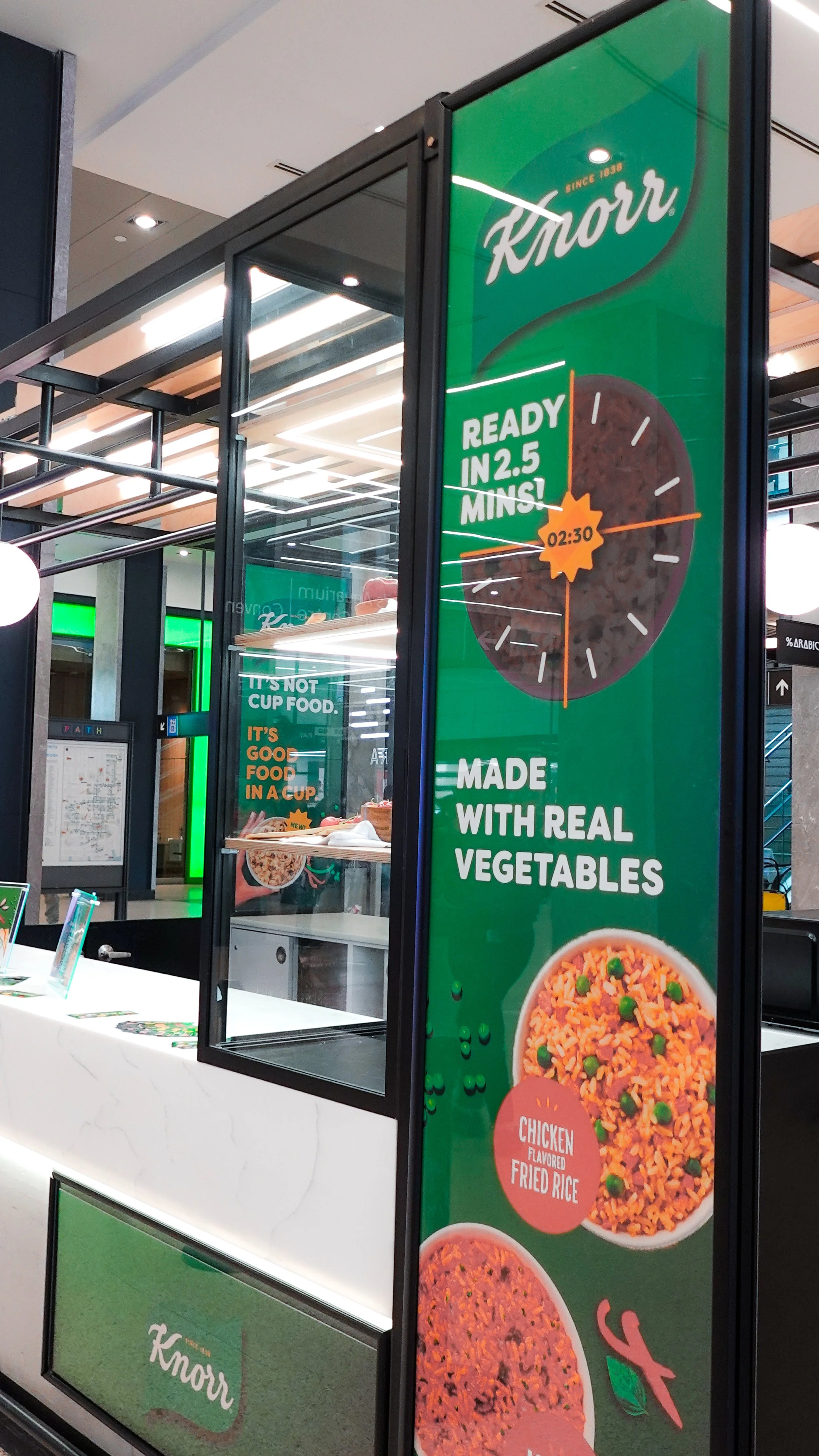A vertical promotional sign for Knorr showing a large clock graphic indicating a 2.5-minute cooking time, with the text 'Made with real vegetables' and an image of fried rice with chicken, designed by Sunnii Studios.