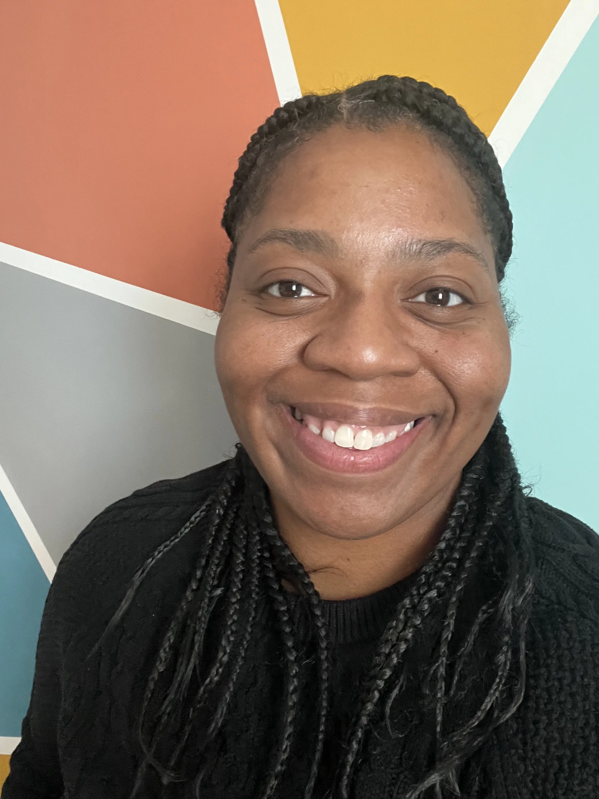 Smiling woman with braided hair in front of a colorful, geometrical background.