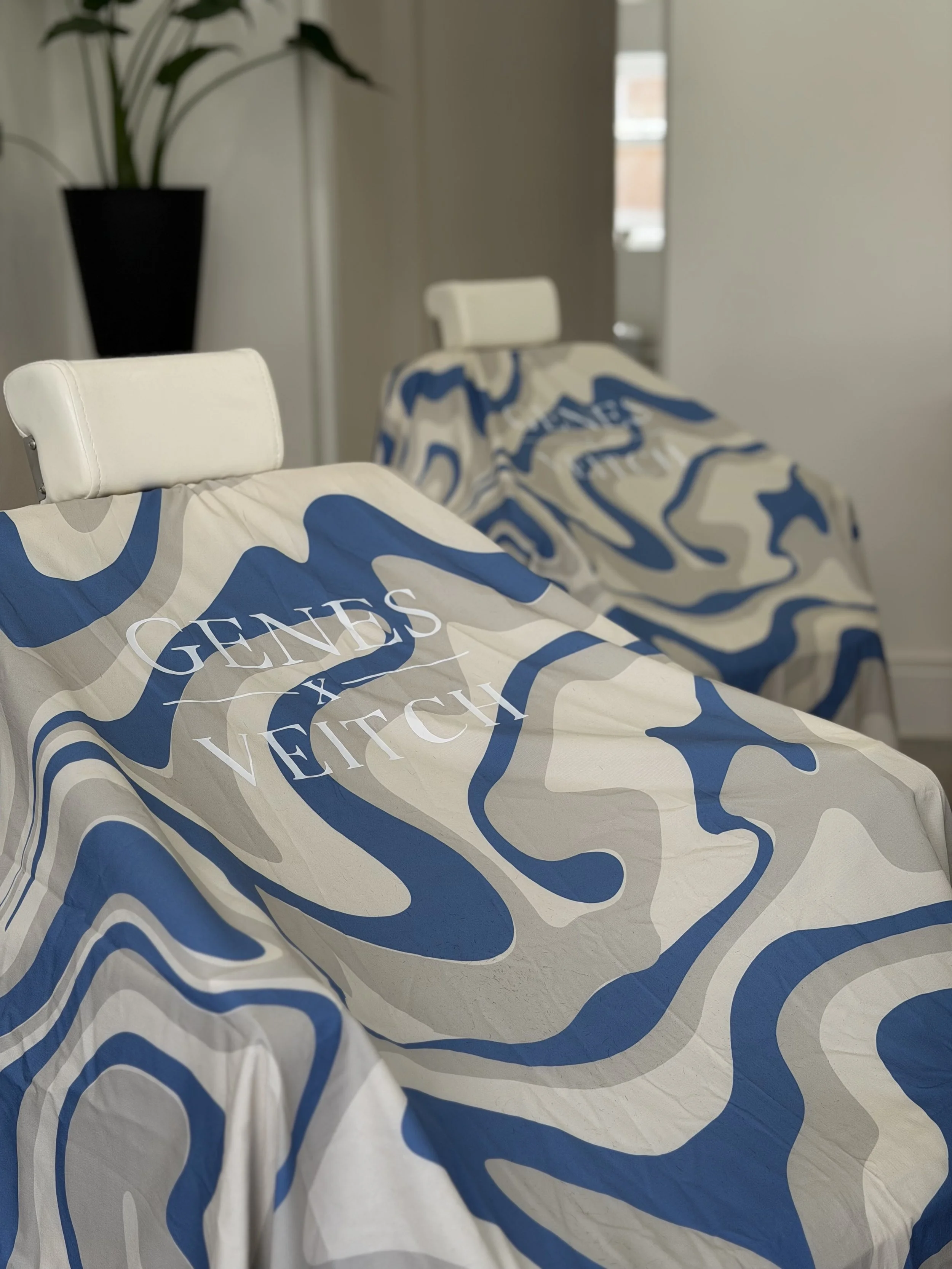 Close-up of gowns with a blue and beige pattern featuring the branding of Genes x Veitch logo.