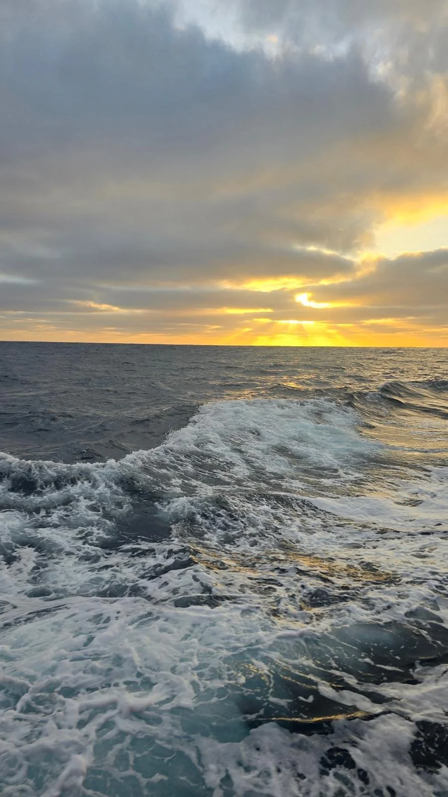 Mar aberta ao pôr do sol com céu parcialmente nublado e ondas na água.