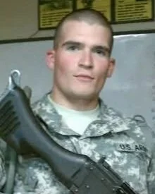 A young man in military uniform holding a firearm.