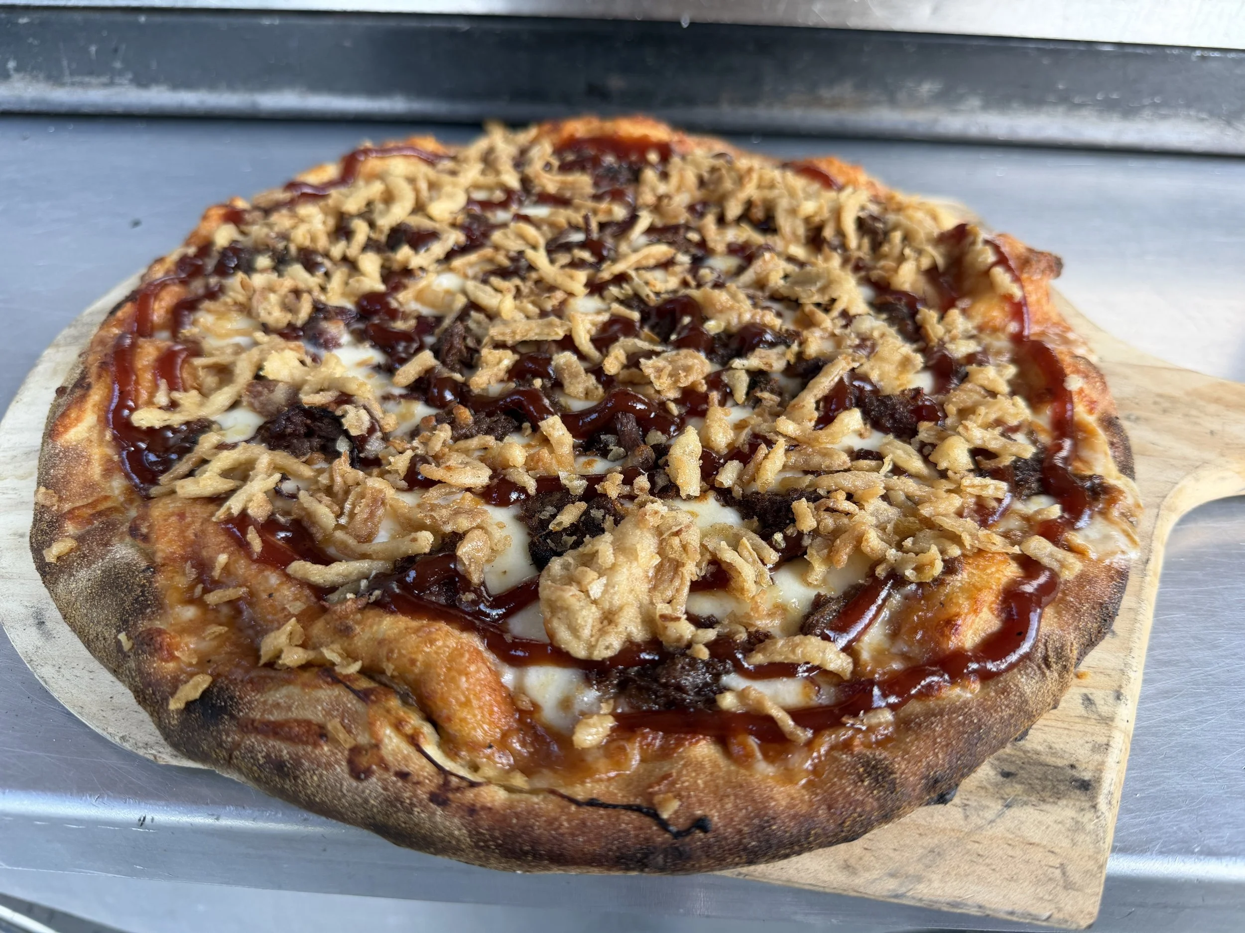 Close-up of a pizza with cheese, grilled chicken, barbecue sauce, and shredded cheese on top, served on a wooden pizza peel.