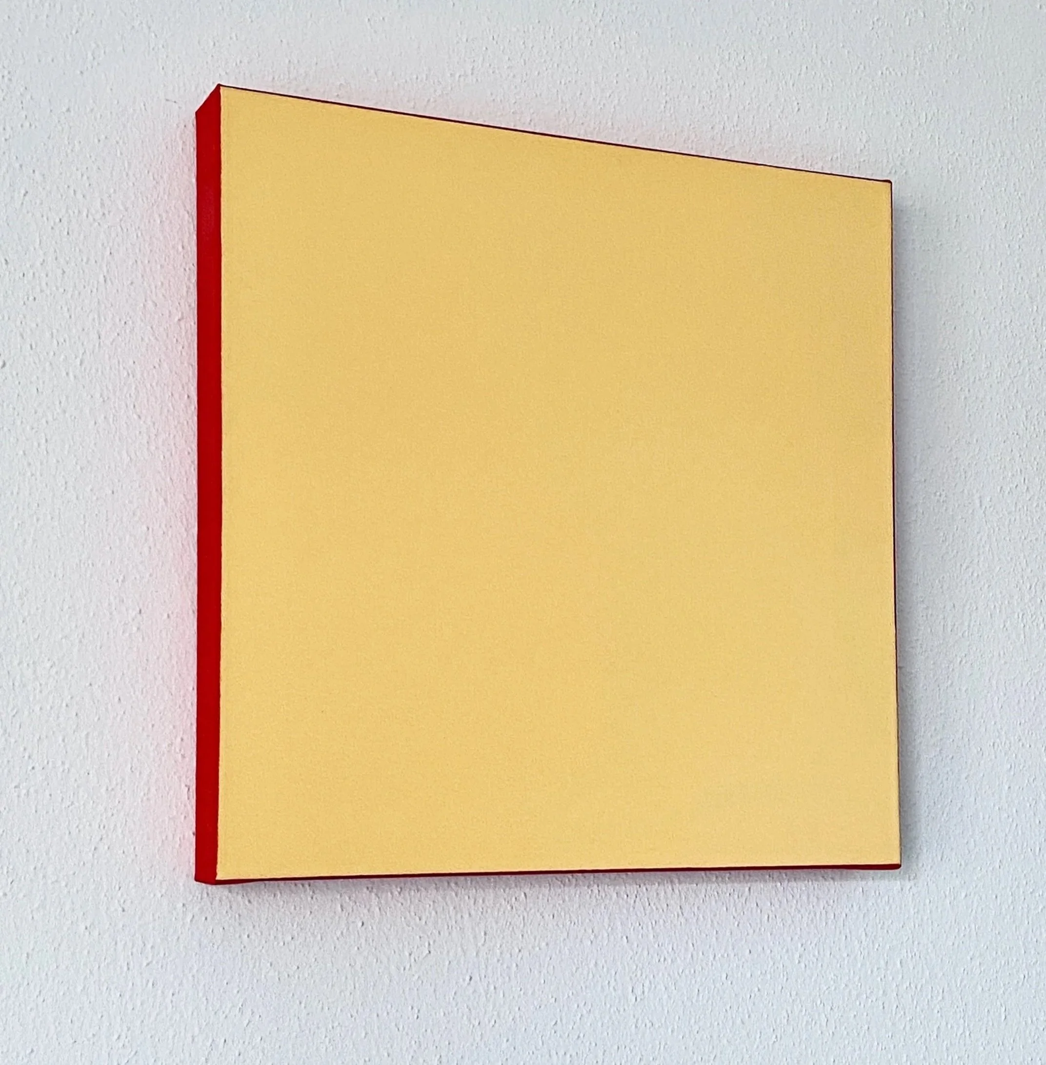 A close-up of a yellow book with a red spine, placed against a white textured wall.