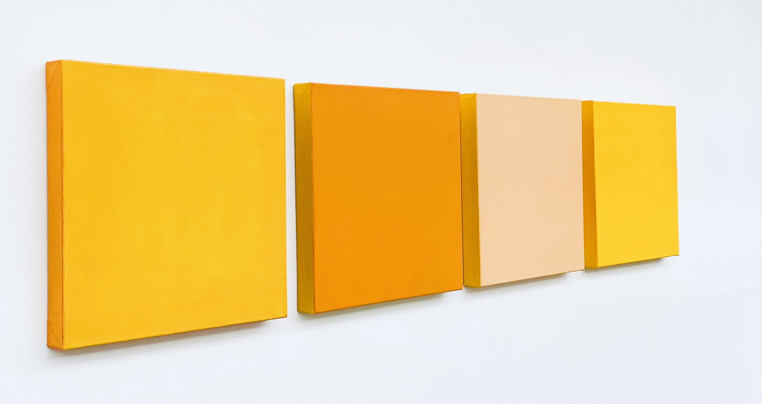Four colorful rectangular blocks mounted on a white wall, ranging from yellow to peach to orange.