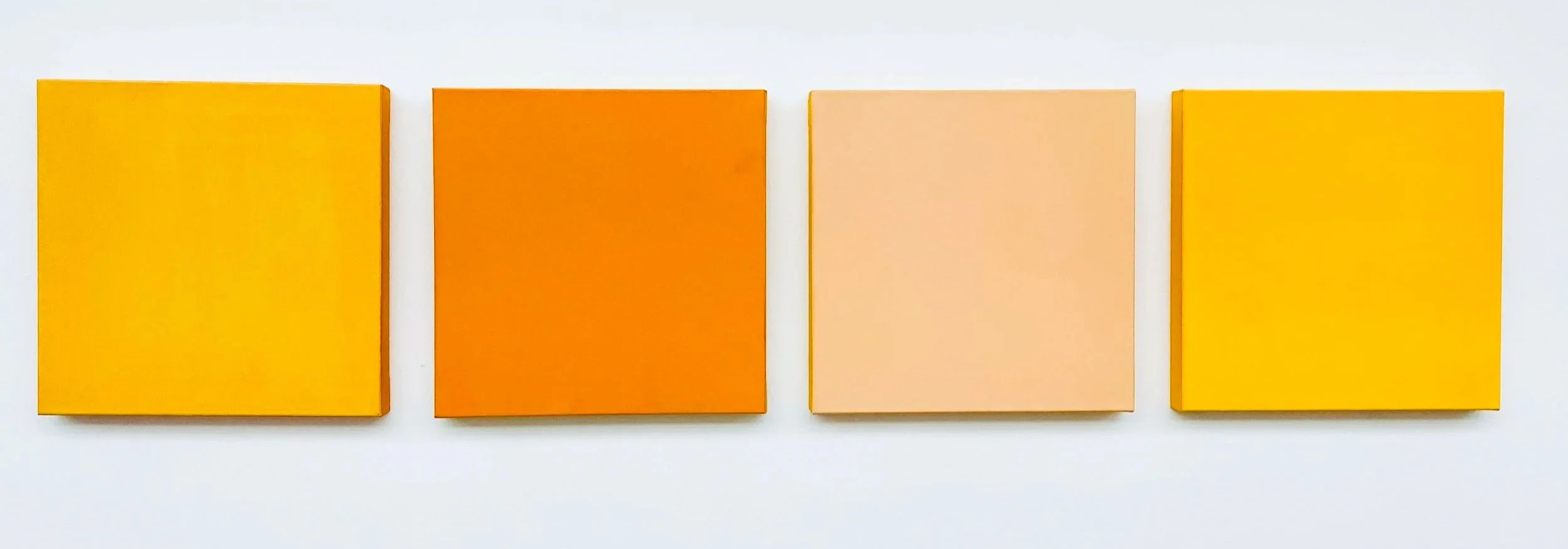 Four square abstract paintings in varying shades of yellow, orange, and peach are hung on a white wall.