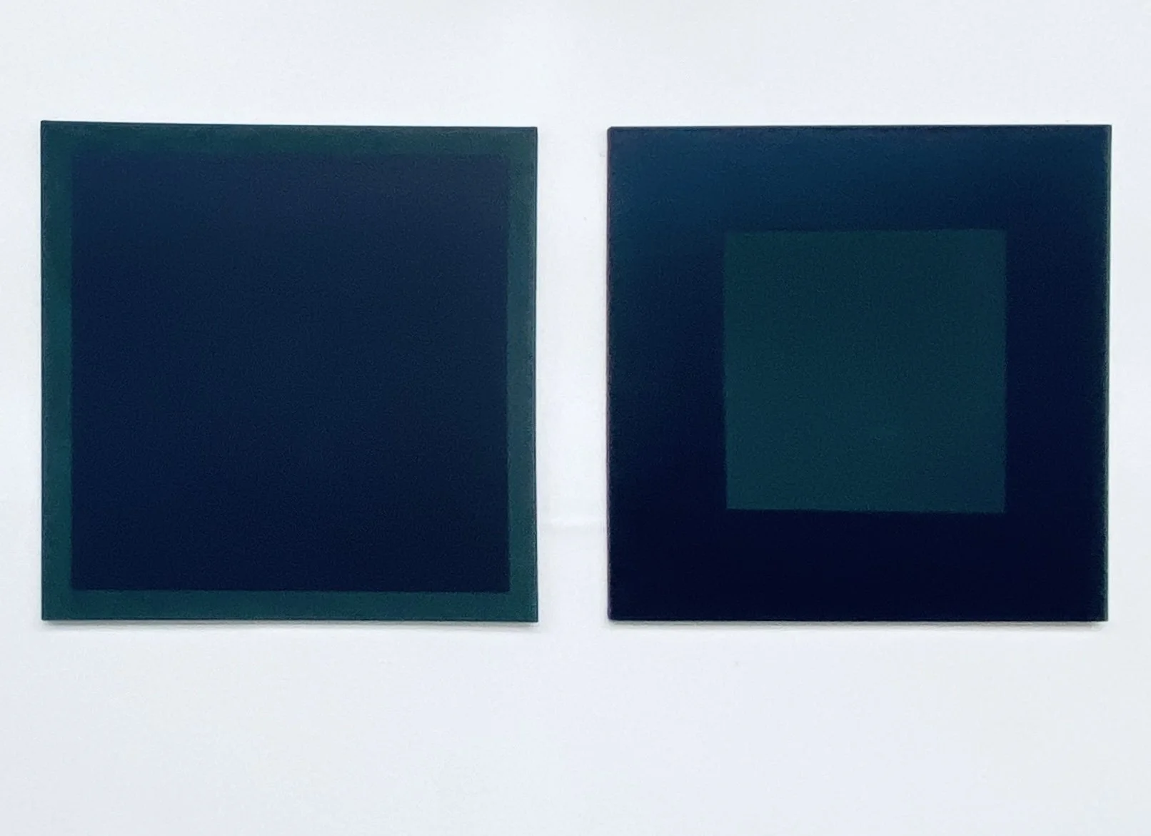 Two dark-colored square objects with a glossy finish, placed side by side on a white background.