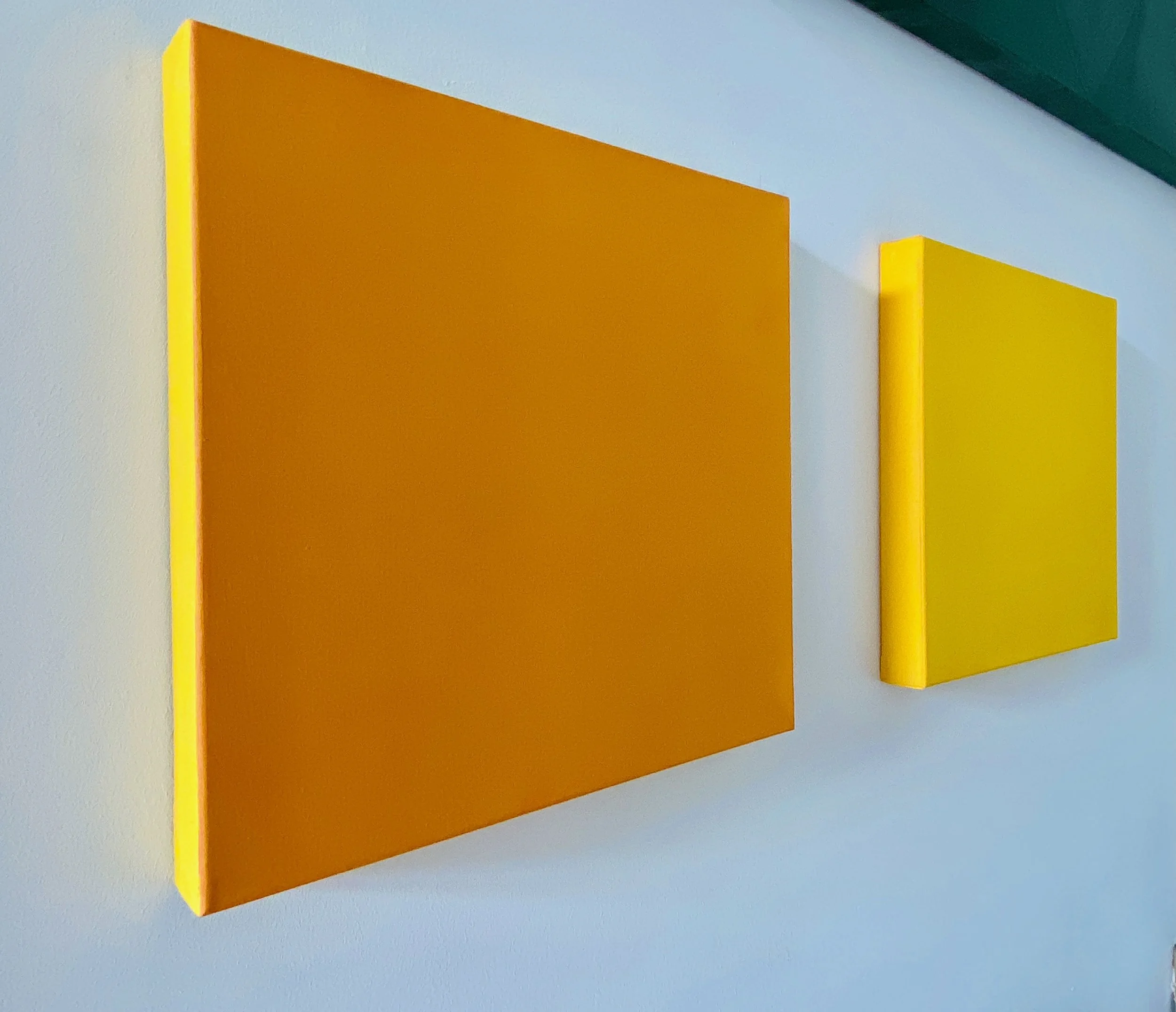 Close-up of three vertically aligned rectangular wall panels in yellow, orange, and yellow, mounted on a white wall with a ledge at the top.