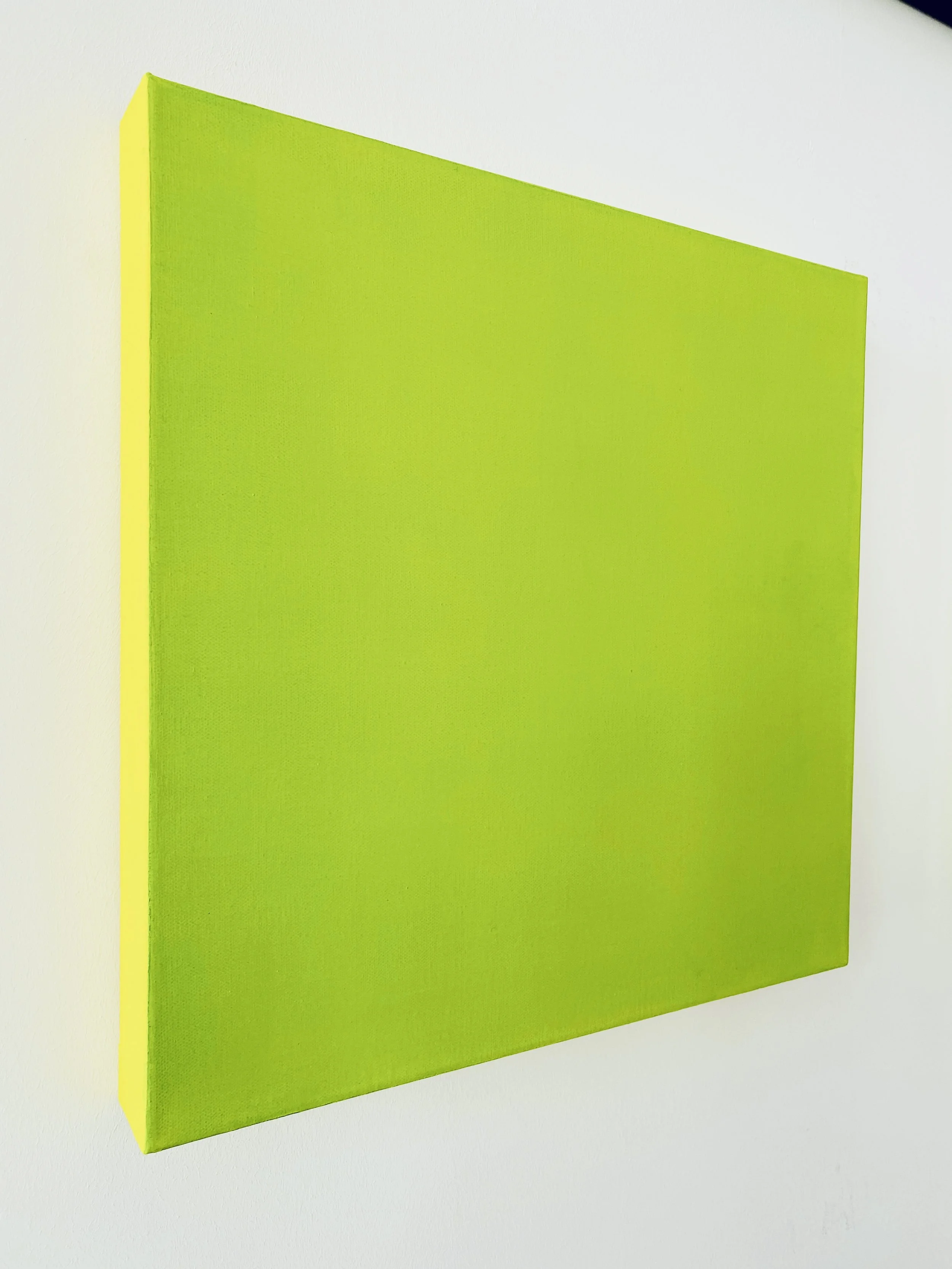 A green canvas panel with a yellow edge hangs on a white wall.