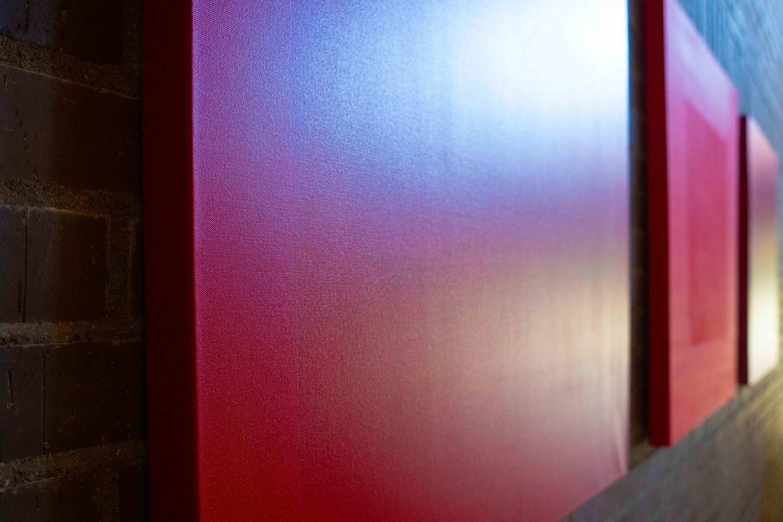 Close-up of colorful panels, possibly part of an art installation or display, with a dark brick wall in the background.