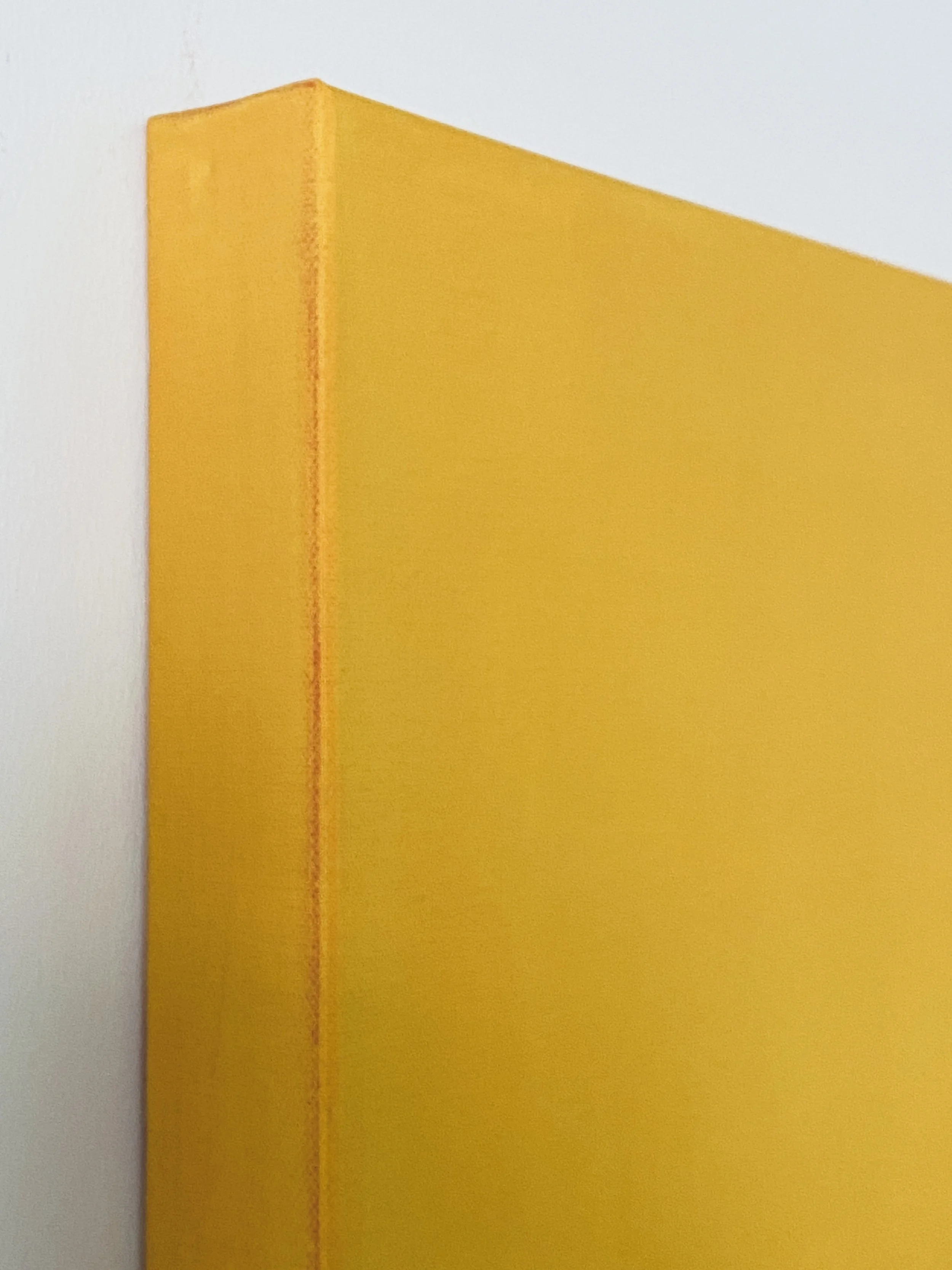 Close-up of a yellow-colored painted wooden corner of a wall with visible brush strokes, against a white background.
