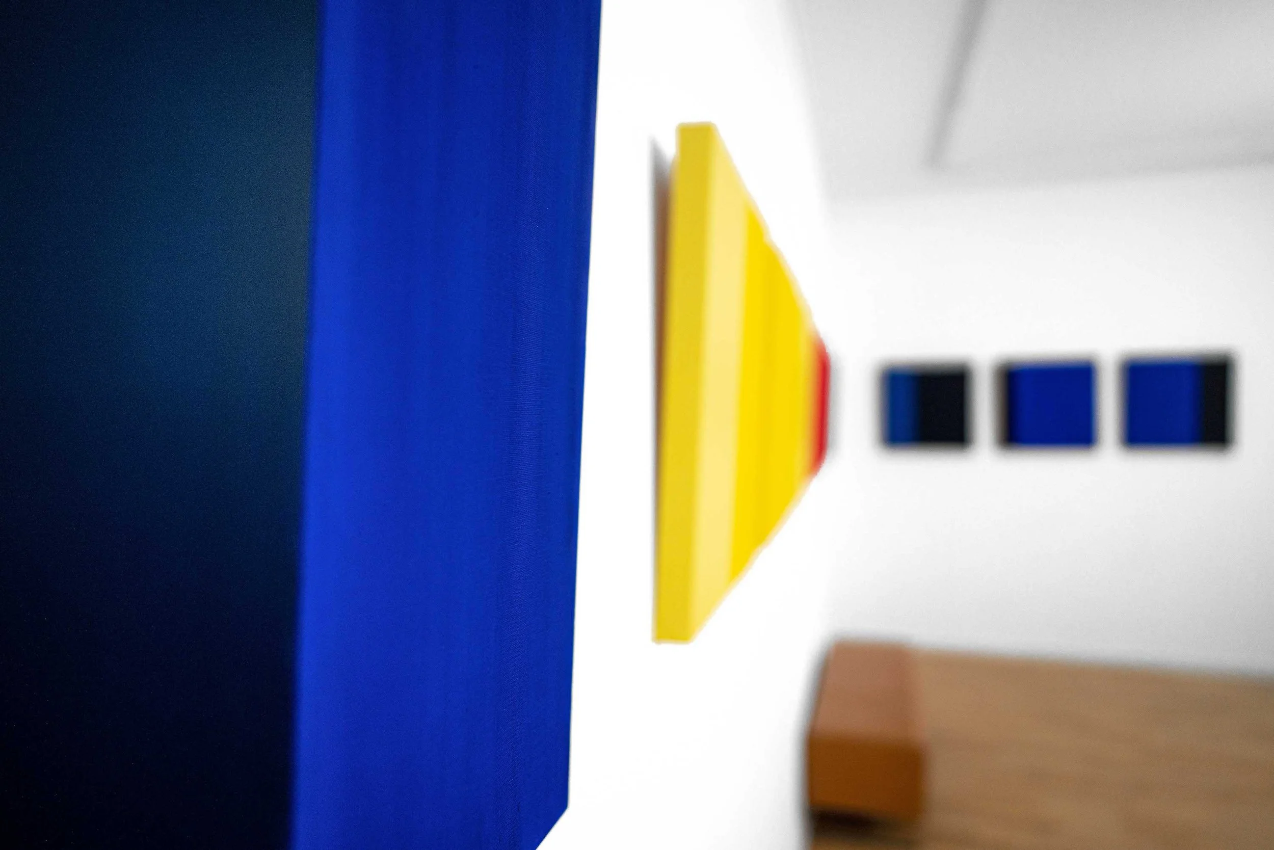 Close-up photograph of a colorful object featuring a prominent blue section, a yellow element, and partial black and white details, with a focus on the blue area and a blurred background.