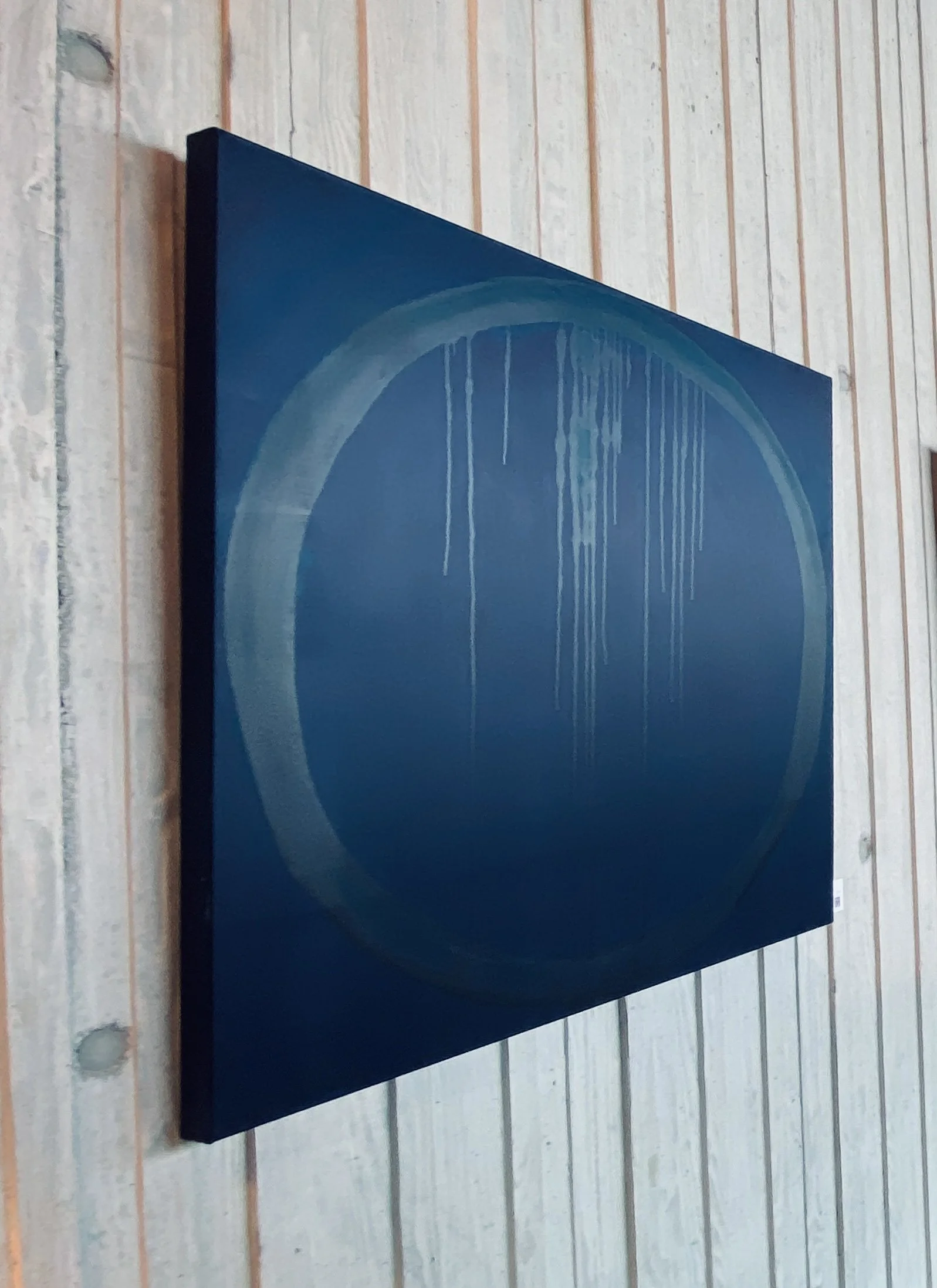 A black speaker with a circular design on the front, mounted on a wooden wall.