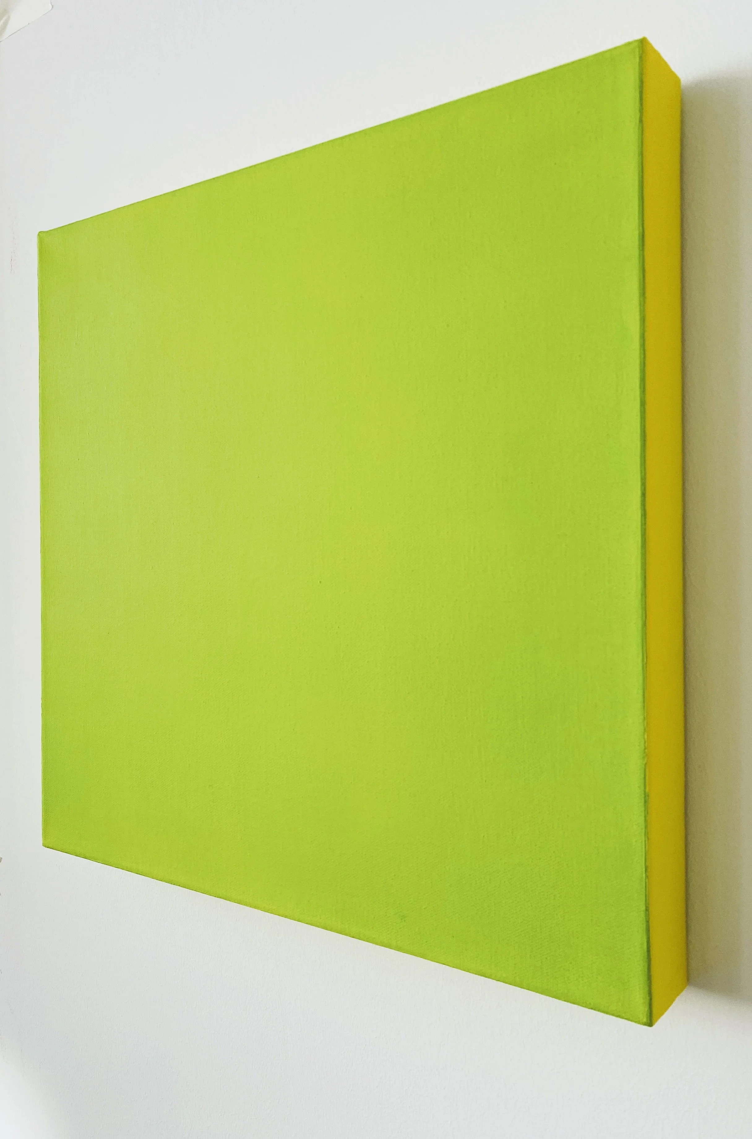 Close-up of a lime green textured canvas mounted on a white wall, viewed from the side.