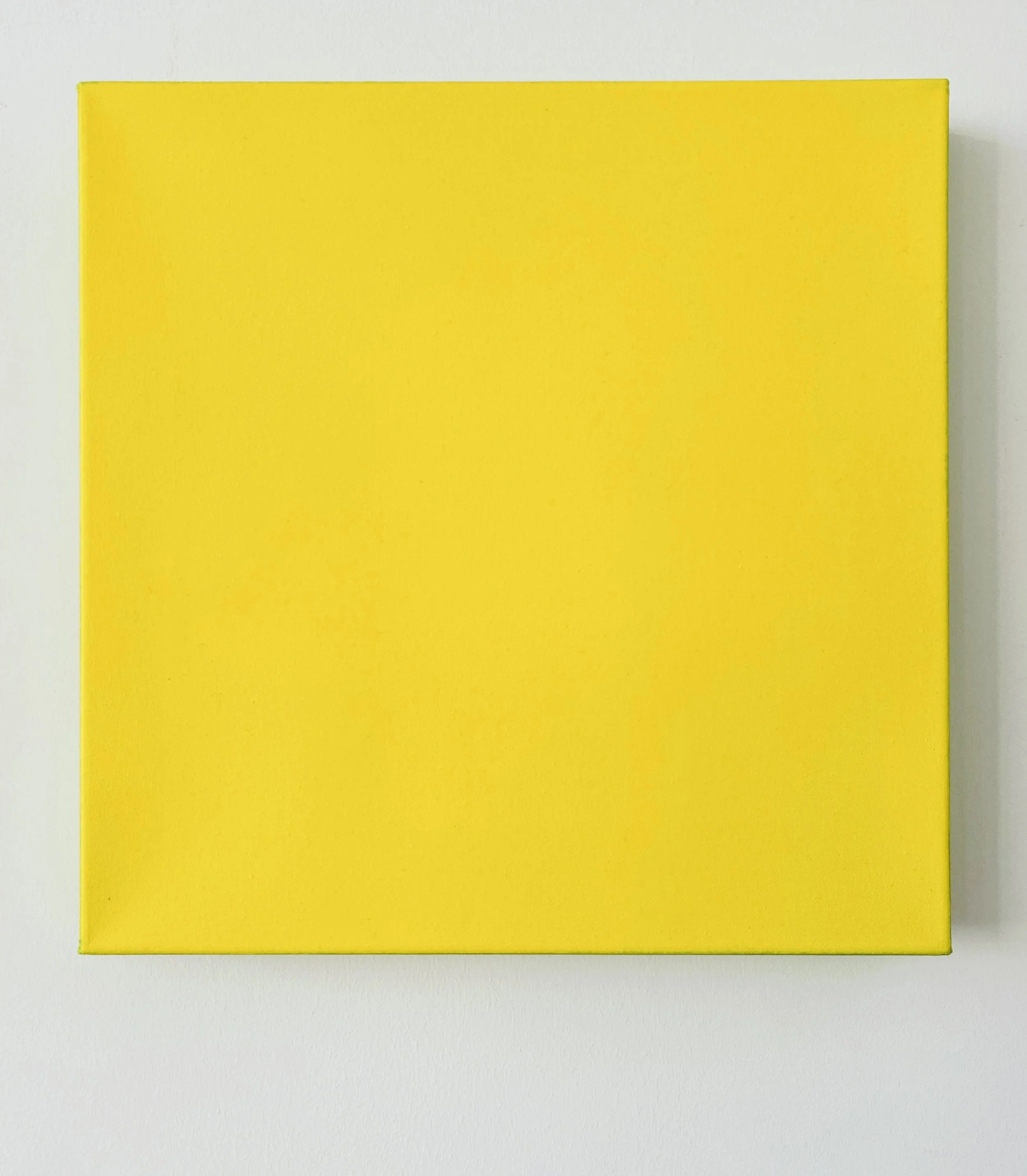 A yellow square canvas mounted on a white wall.