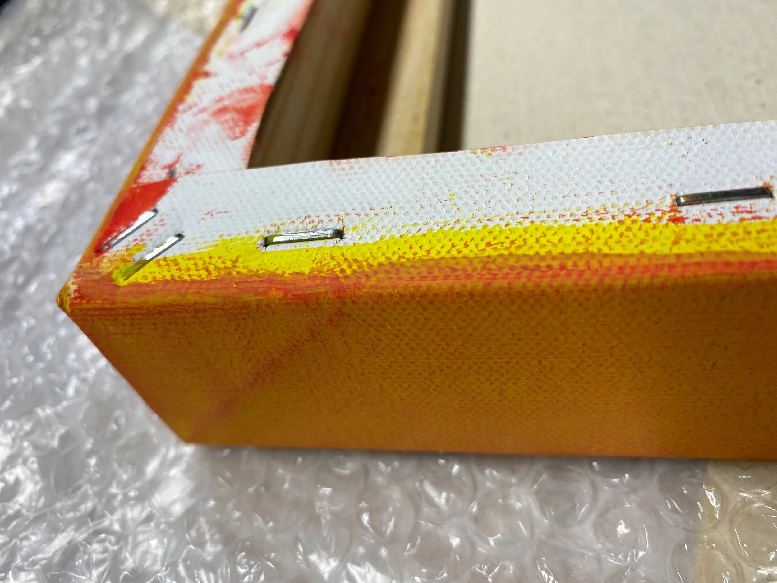 Close-up of a yellow and white cardboard box with metal staples, resting on bubble wrap.