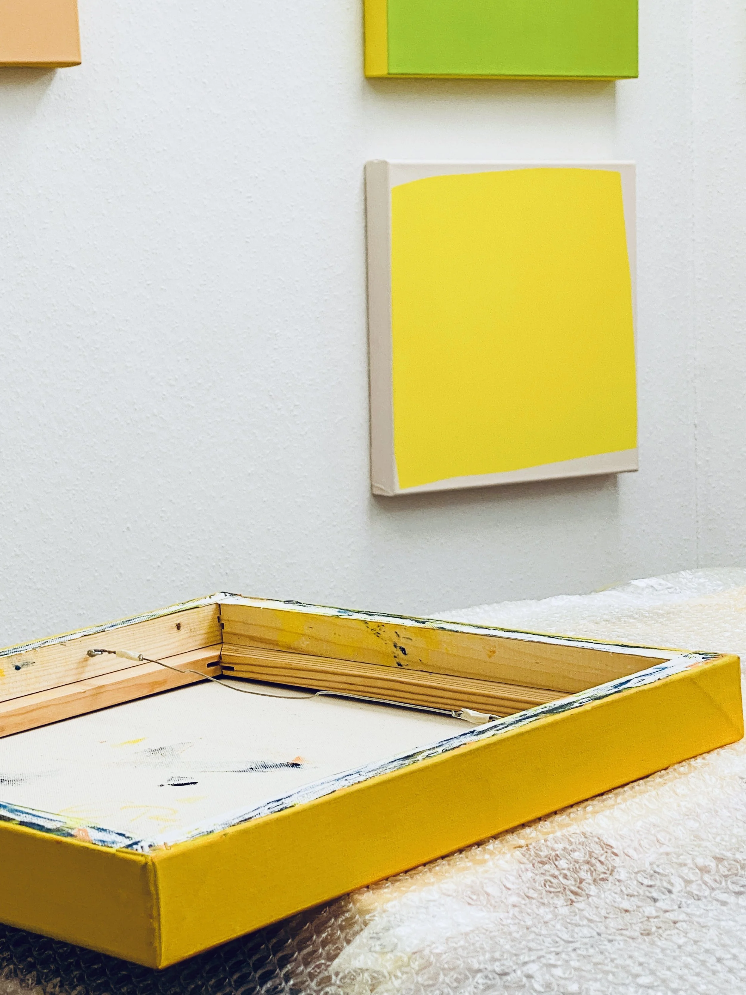 Unfinished wooden picture frame inside a yellow box with paint on the edges, placed on a textured white surface.