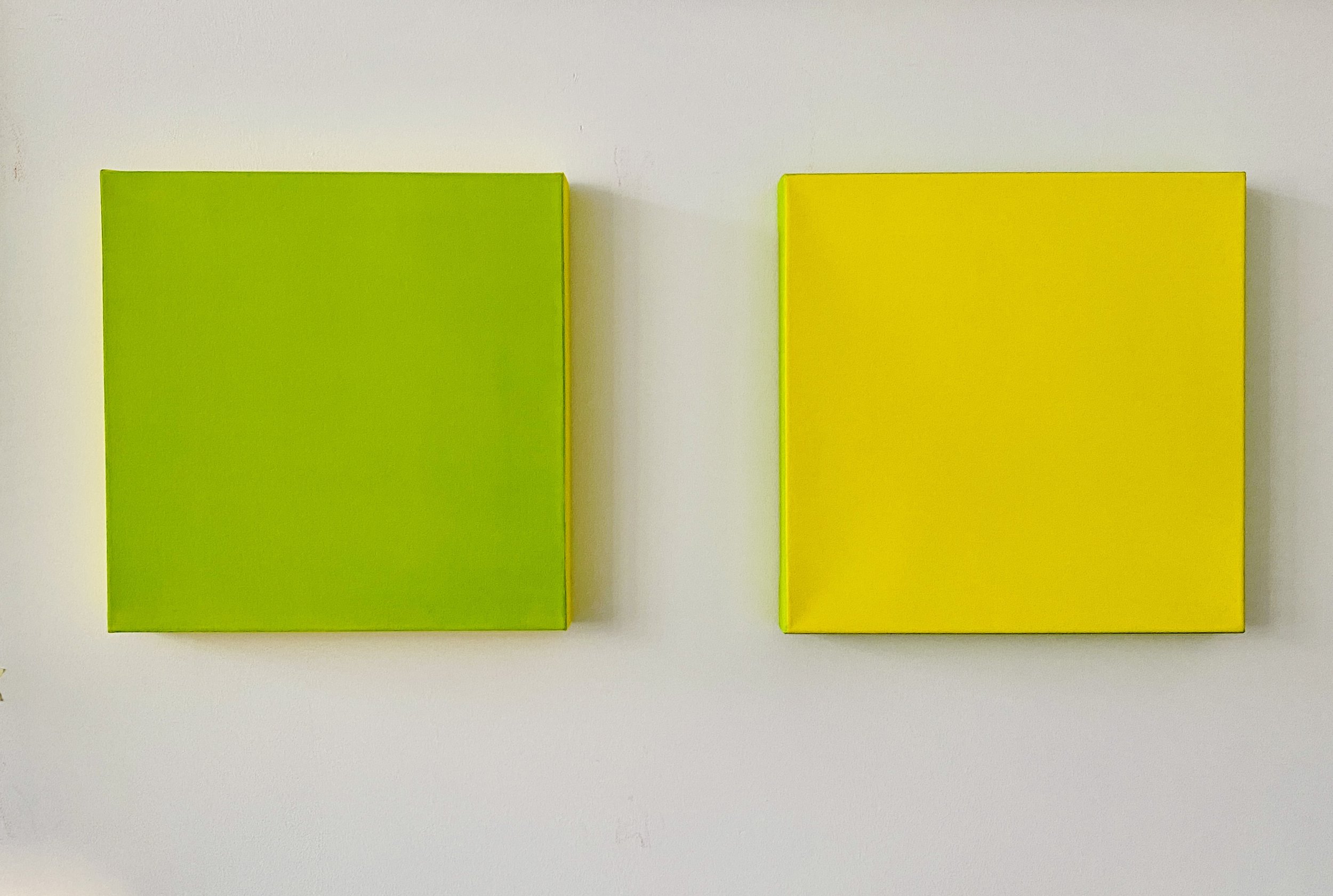Two rectangular blocks, one green and one yellow, mounted on a white wall with the green block on the left and the yellow block on the right.