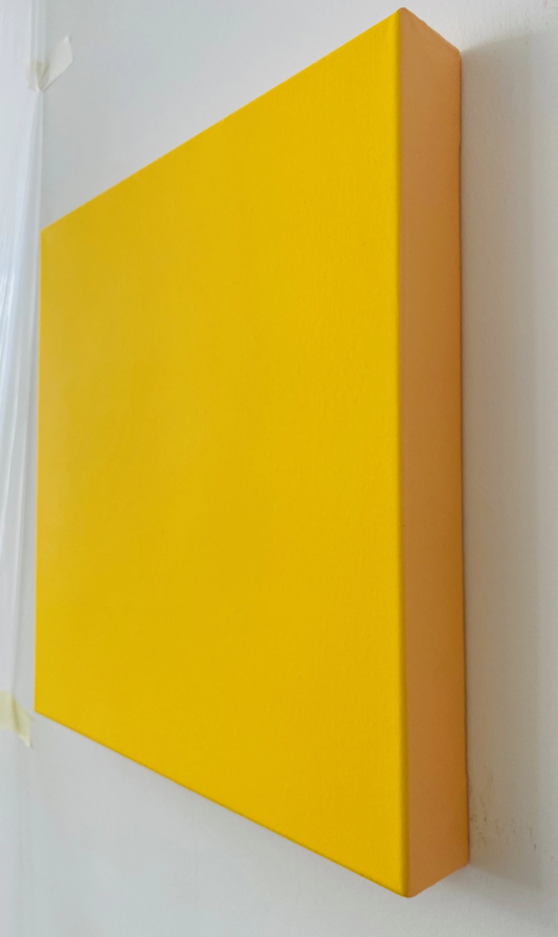 A rectangular canvas with a yellow horizontal stripe on the top third and a orange vertical stripe on the right side, placed on a white wall.