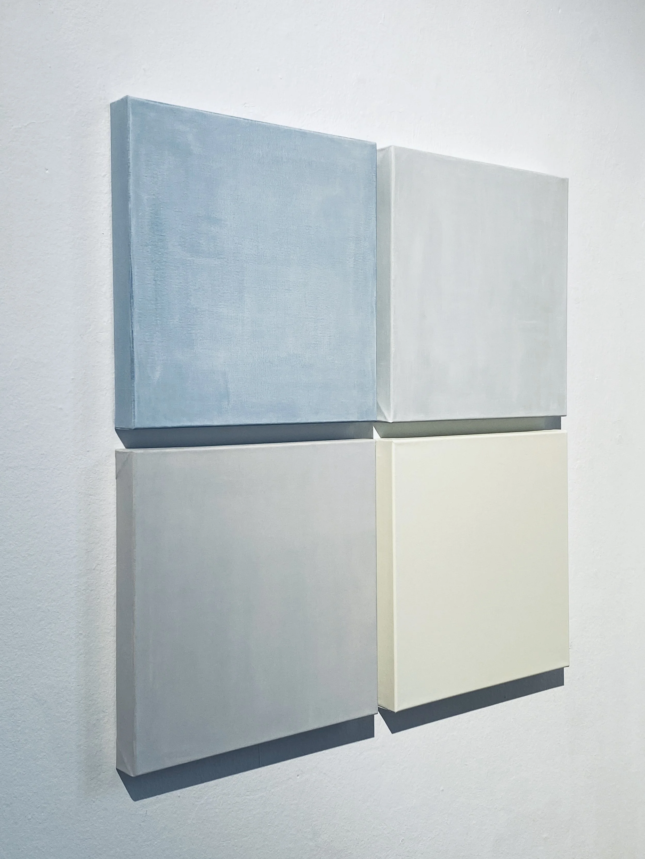 Two minimalist canvases mounted on a white gallery wall, painted in soft pastel blue and off-white colors.