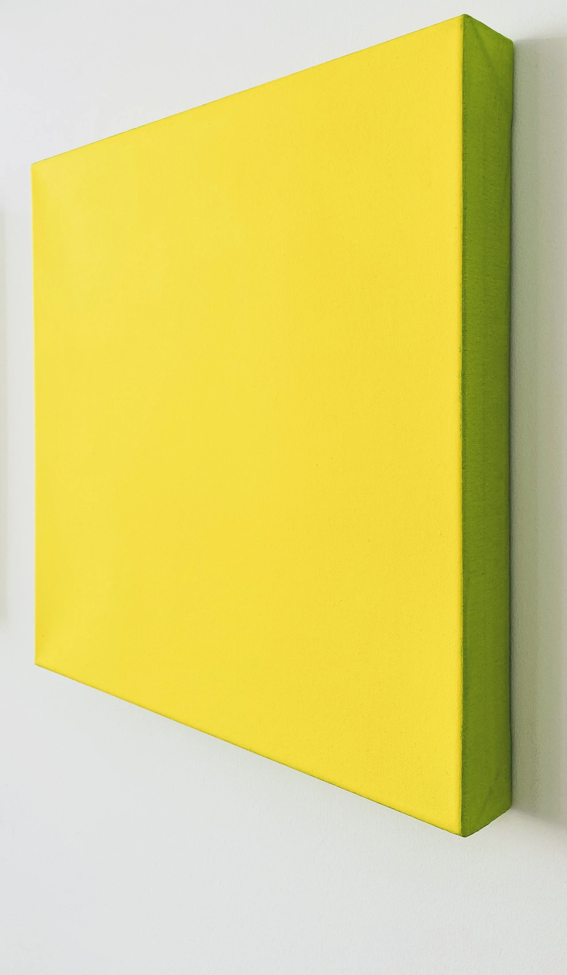 A square, yellow canvas with a green edge, mounted on a white wall.