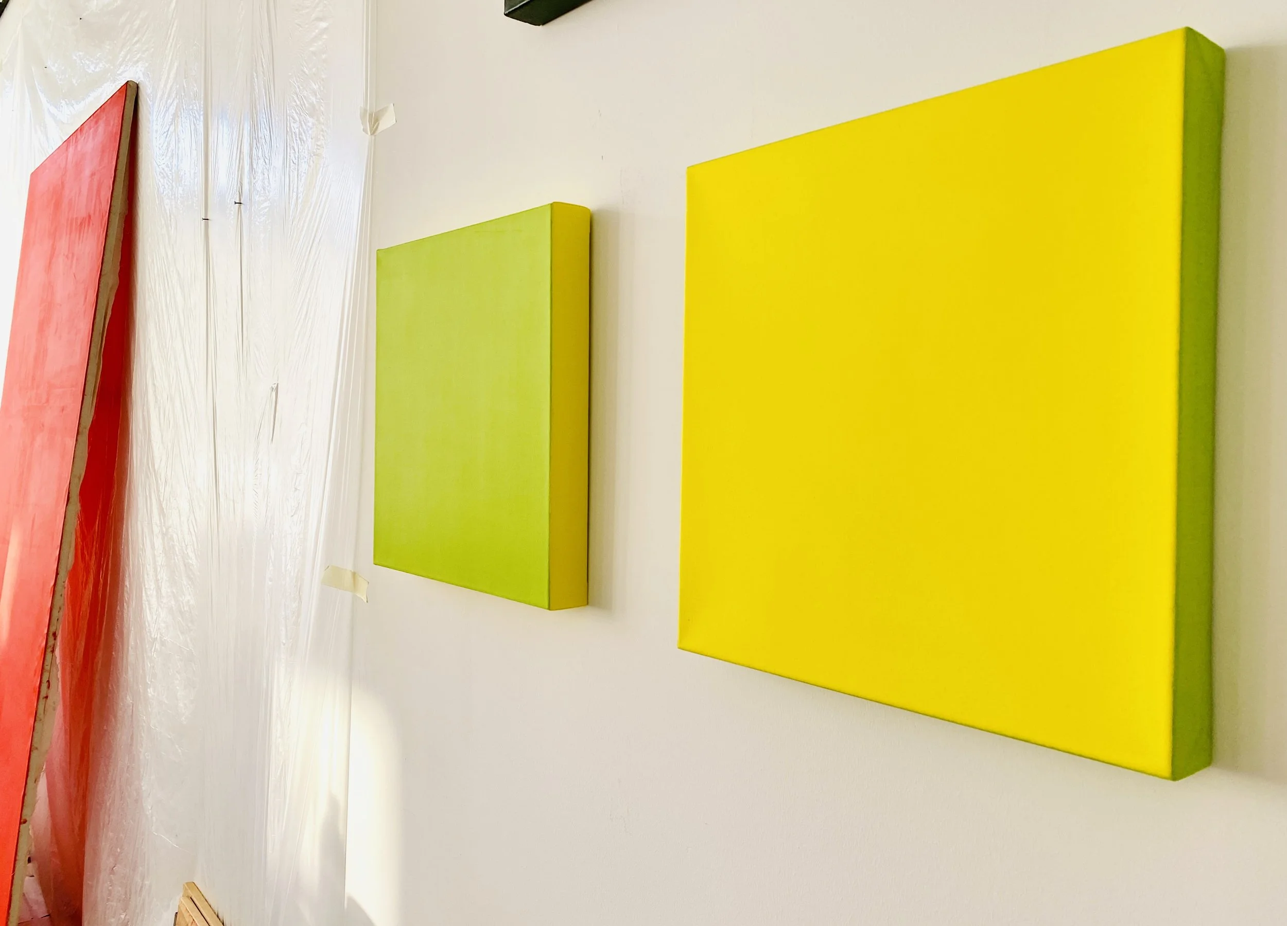 Colorful abstract paintings on a white wall, featuring red, green, and yellow sections.