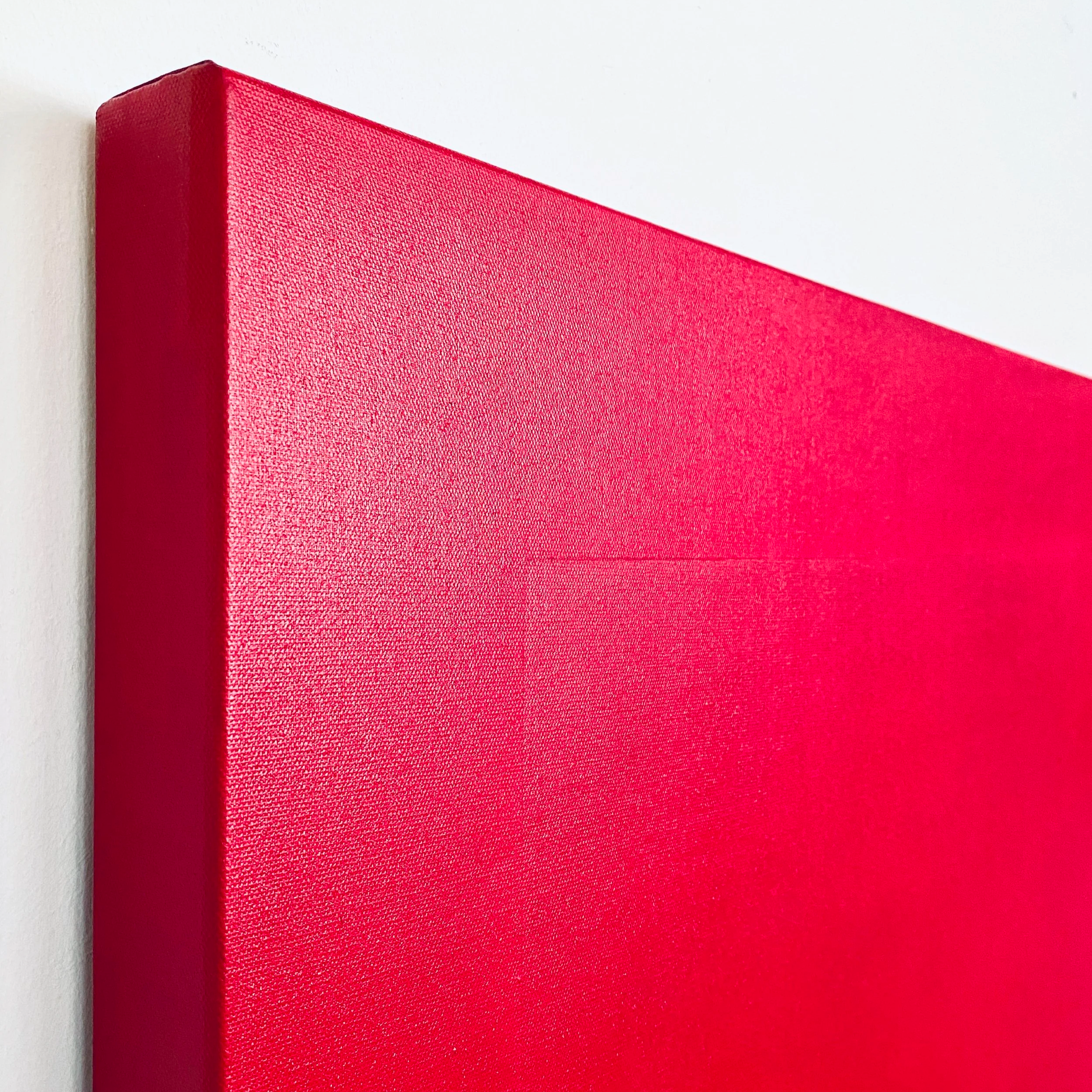 Close-up of a red canvas with textured fabric, mounted on a white wall.