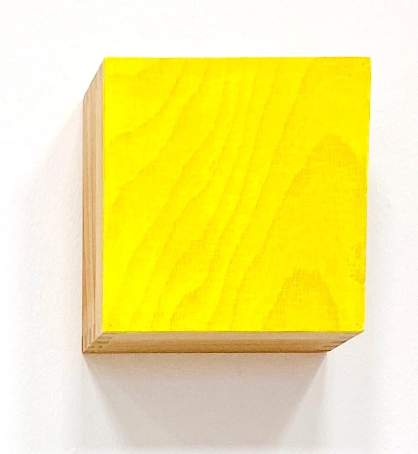 A wooden box with a yellow painted lid hanging on a white wall.