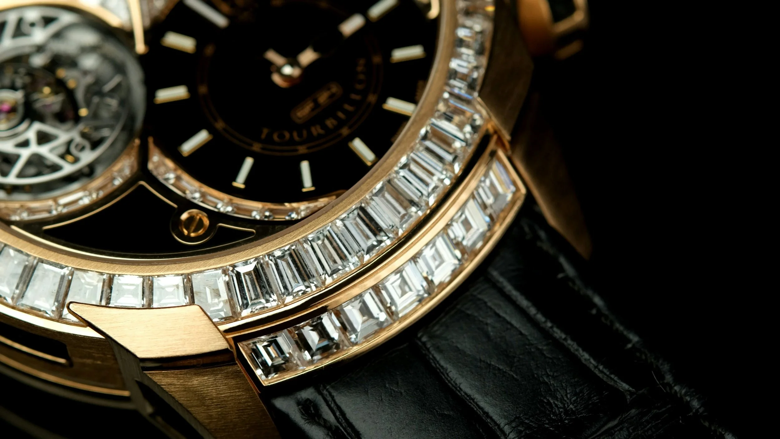 Nahaufnahme einer luxuriösen Armbanduhr mit goldfarbenem Gehäuse, main goldener Lünette mit eingearbeiteten Diamanten, schwarzem Zifferblatt und einem sichtbar schwingenden Tourbillon. Die Uhr liegt auf schwarzem Leder und zeigt Details wie das Zifferblatt, das Tourbillon und die Diamanten an der Lünette.