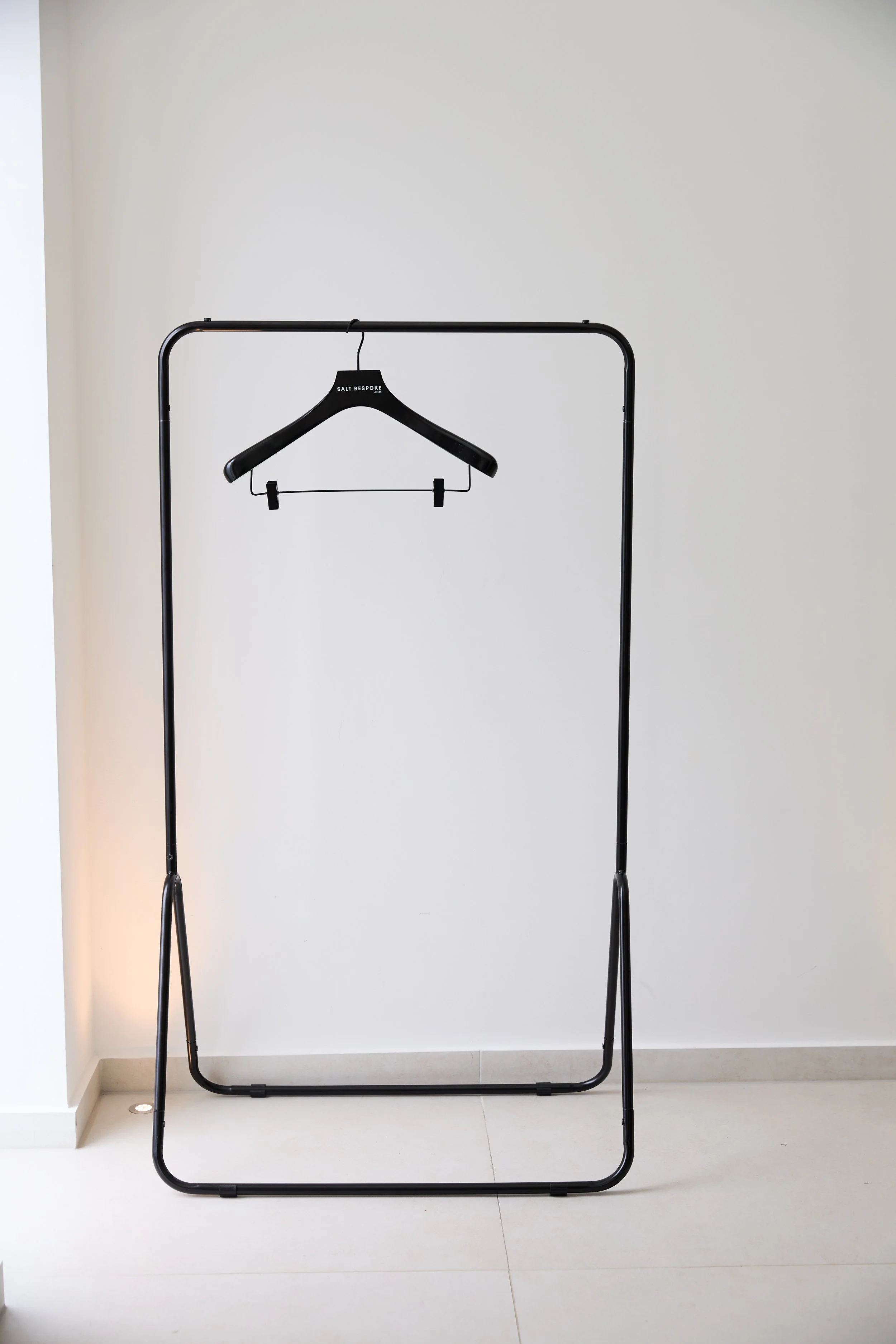 A branded black salt bespoke suit hanger, hanging on a black clothing rail against a crisp white background