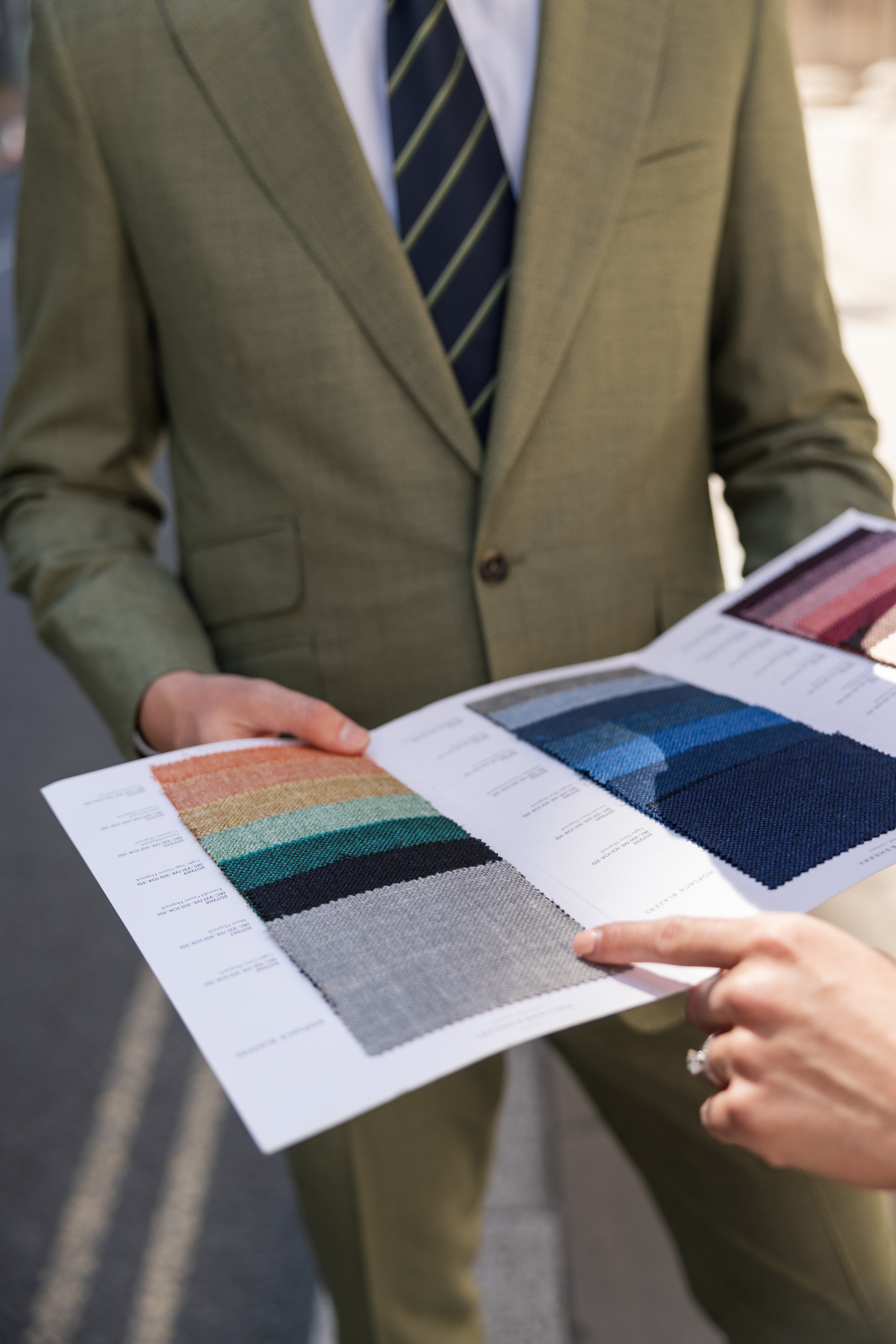 Ian Powell showing a client fabric swatches to a client wearing a bespoke mid green suit