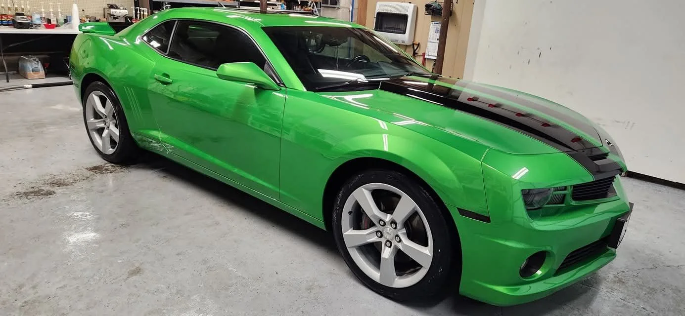 A green sports car with a black racing stripe running along the center of the hood, freshly detailed both interior and exterior.