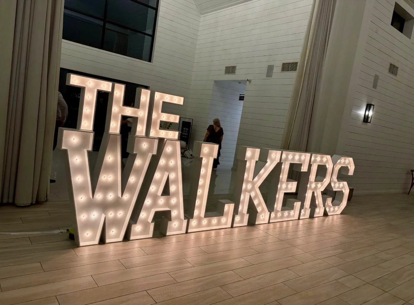Large decorative sign spelling 'THE WALKERS' with illuminated letter lights in a modern, white-walled interior space.