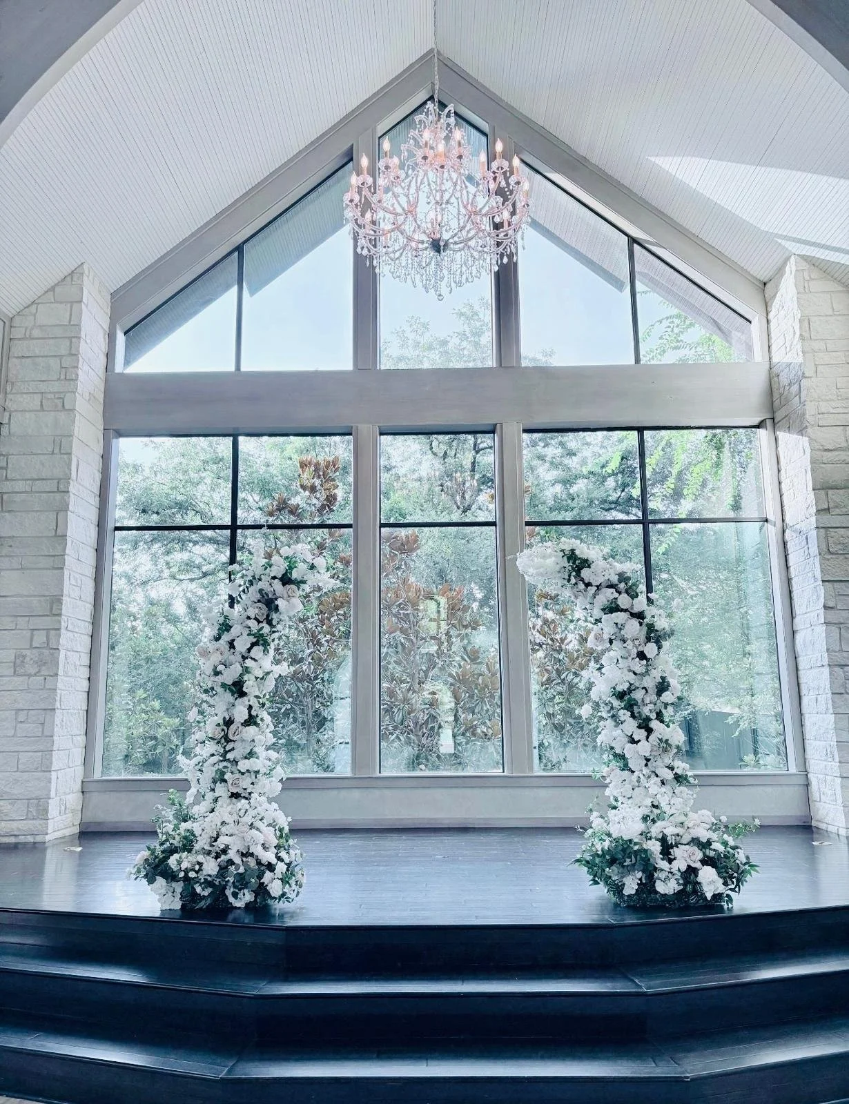 Large window with white floral arrangements on either side and a chandelier hanging from the ceiling.
