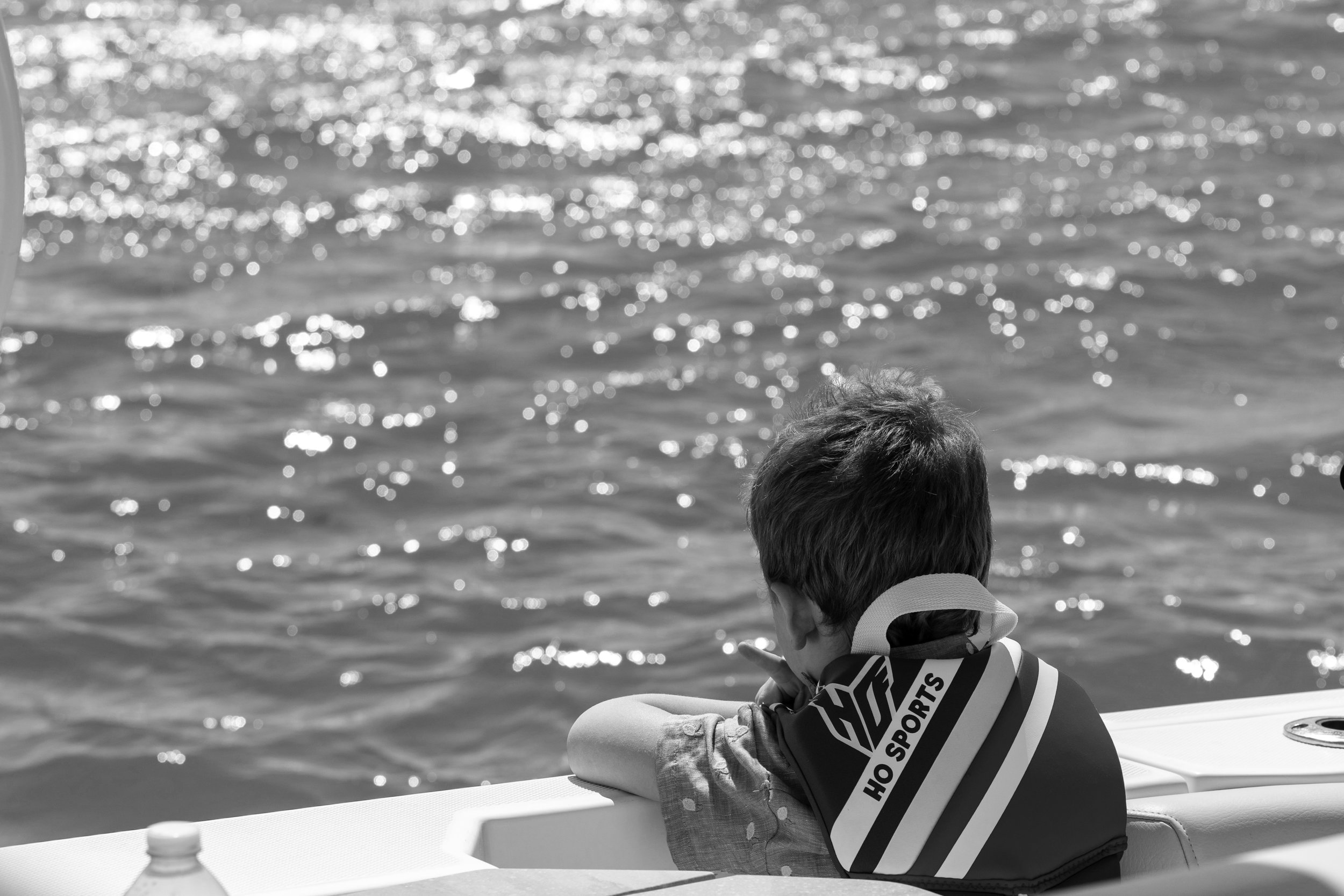 Child sitting on a boat, looking at the water, with sunlight reflecting on the surface.