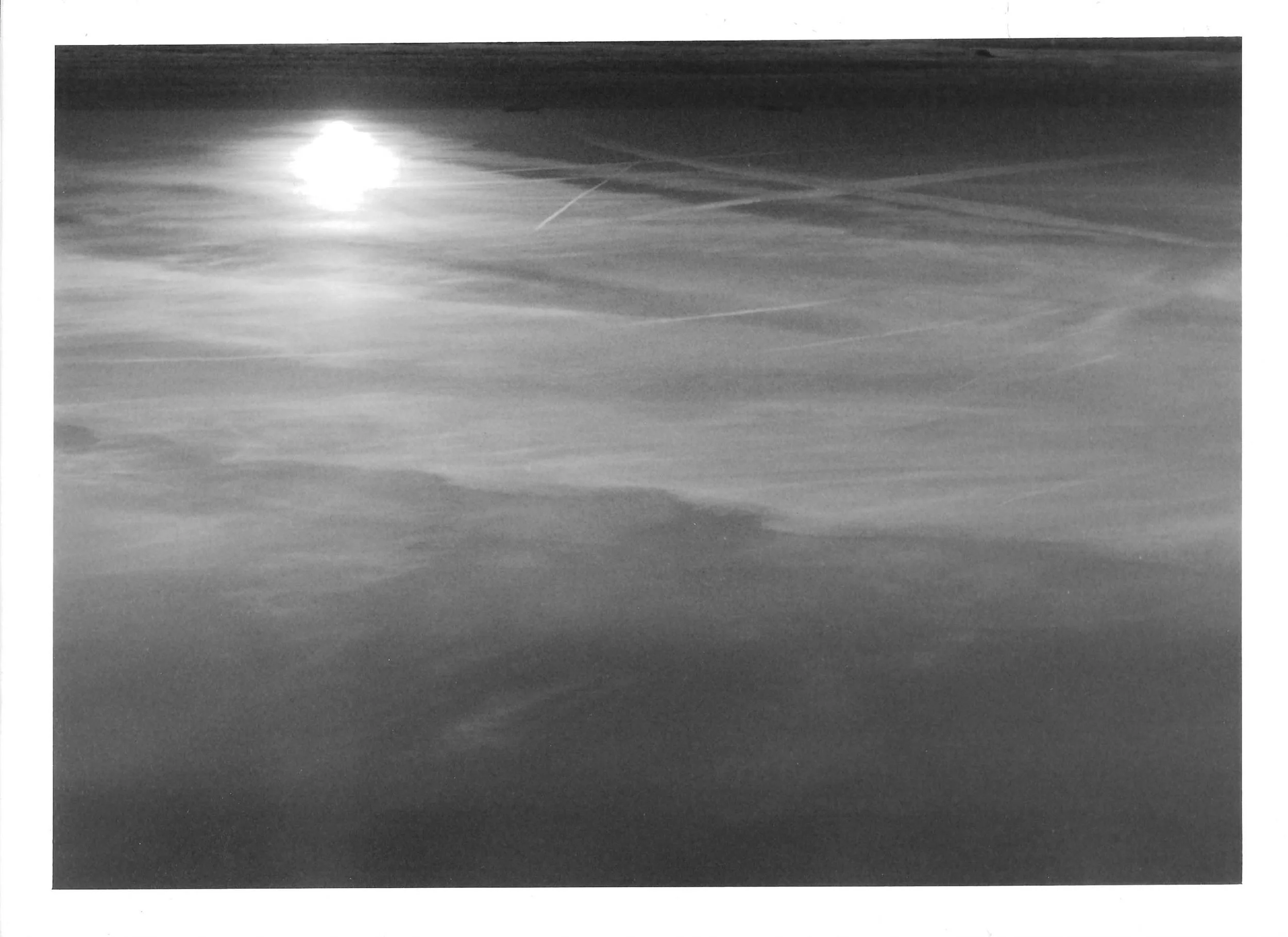 Fotografia analógica em preto e branco, integrante da Série 3, de Sandra Unglert Fernandes, mostrando um foco de luz refletido sobre uma superfície, com tonalidades e transparências que lembram uma aquarela.