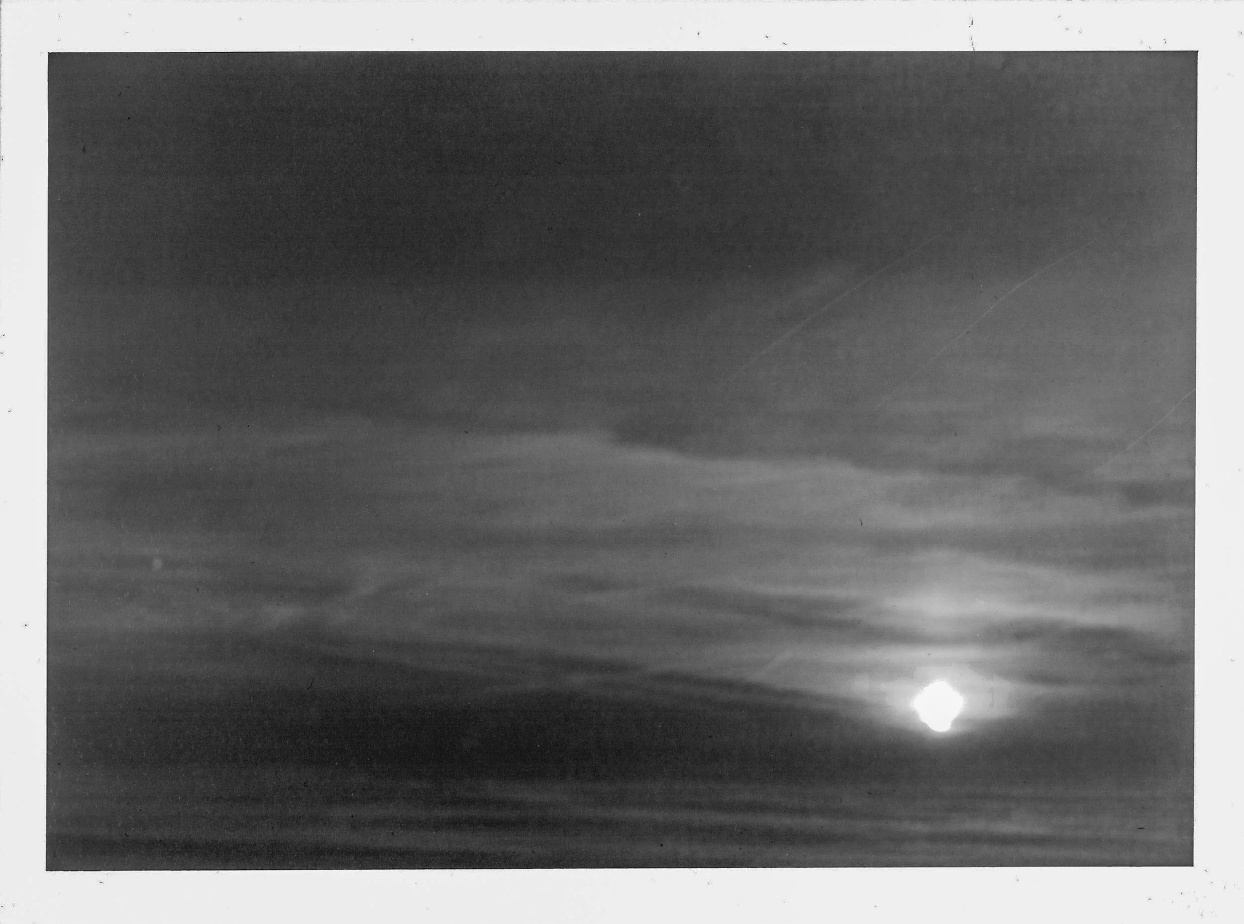 Fotografia analógica em preto e branco da Série 1, de Sandra Unglert Fernandes, mostrando o sol próximo ao horizonte sobre o mar.