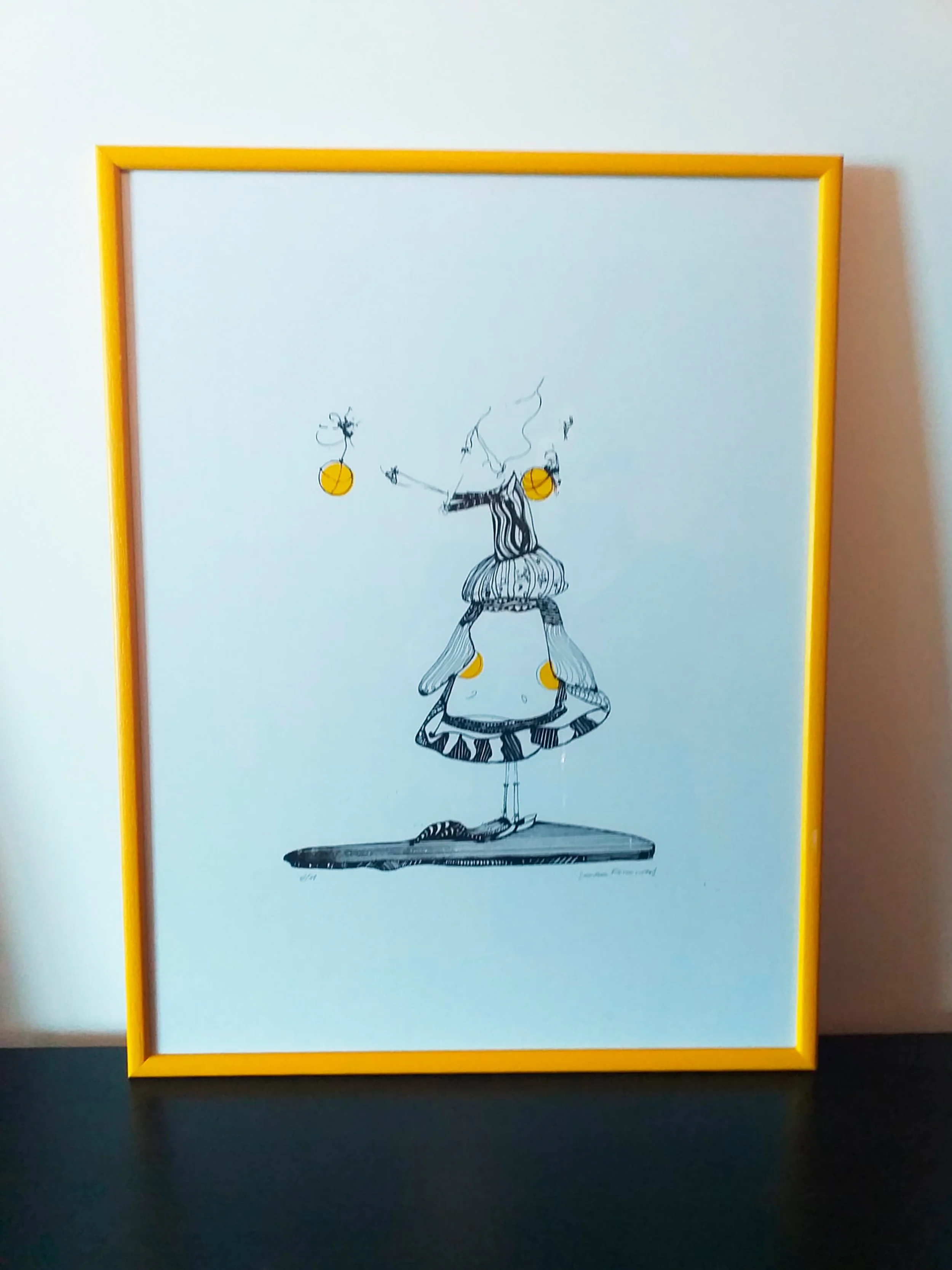 Serigrafia de Sandra Unglert Fernandes emoldurada, mostrando uma figura humana estilizada acompanhada por quatro círculos amarelos sobre fundo branco.