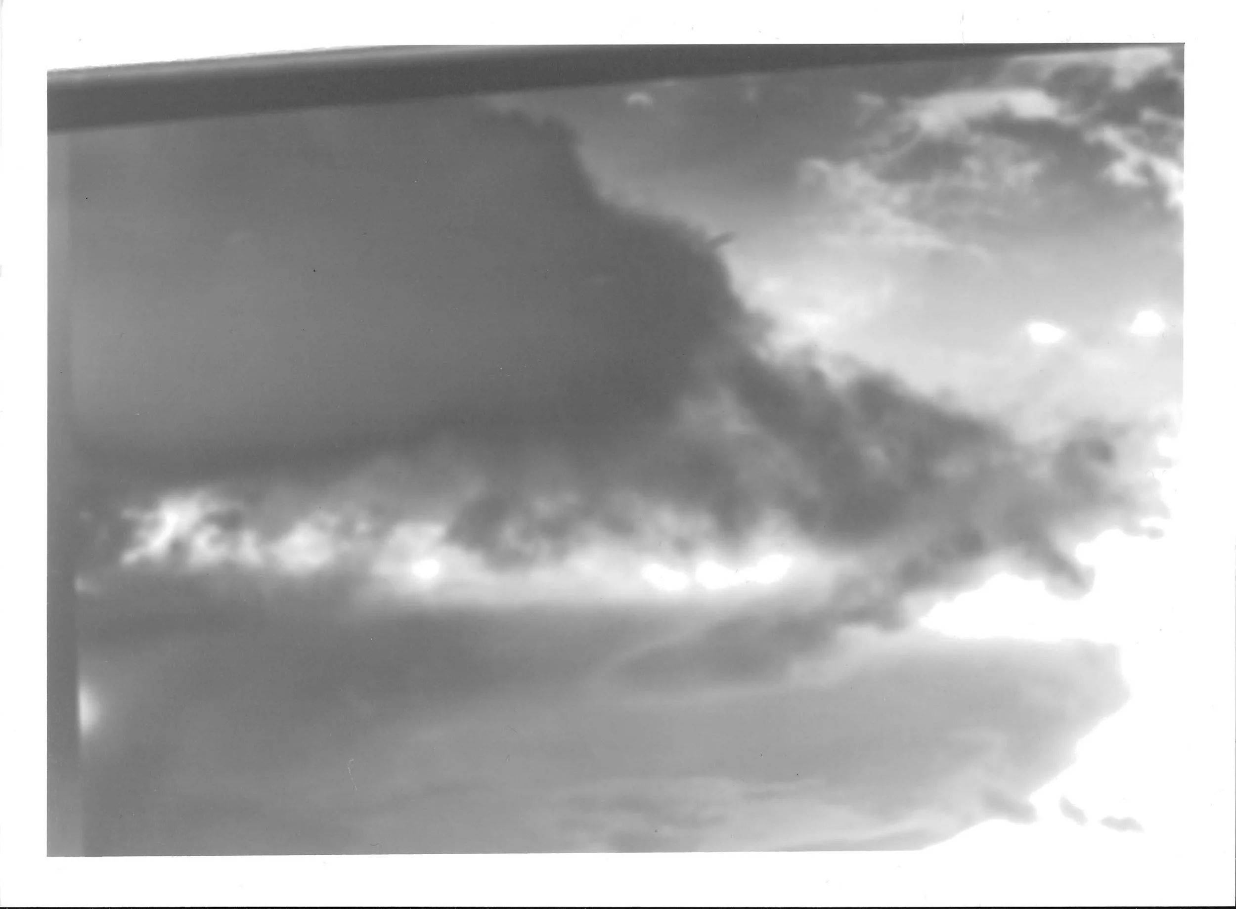 Fotografia analógica em preto e branco, integrante da Série 2, de Sandra Unglert Fernandes, mostrando formações de nuvens escuras iluminadas pela luz entre suas aberturas.