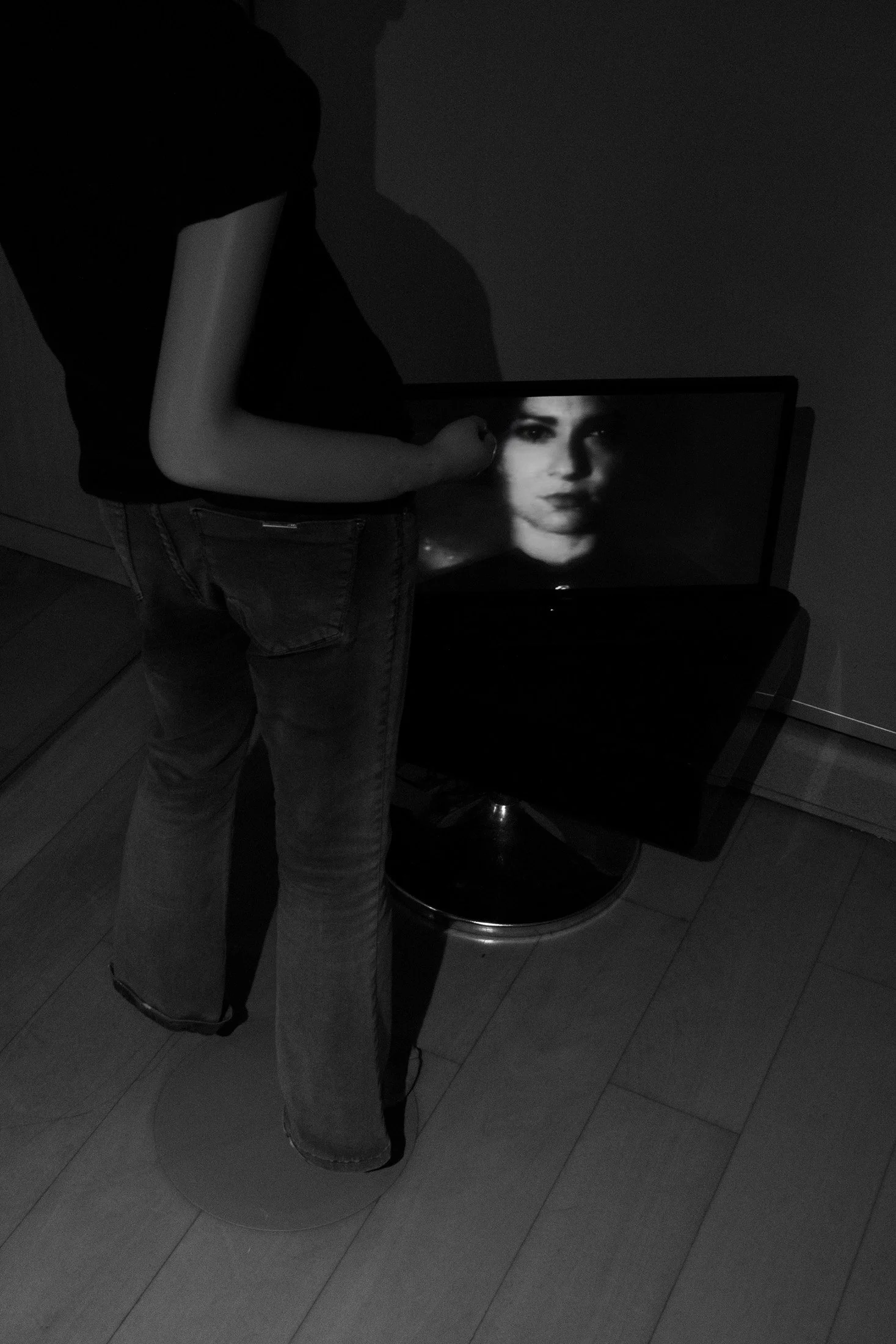 Fotografia digital em preto e branco, integrante da Série Digital 1, de Sandra Unglert Fernandes, mostrando uma pessoa de costas diante de um monitor com um retrato em preto e branco.
