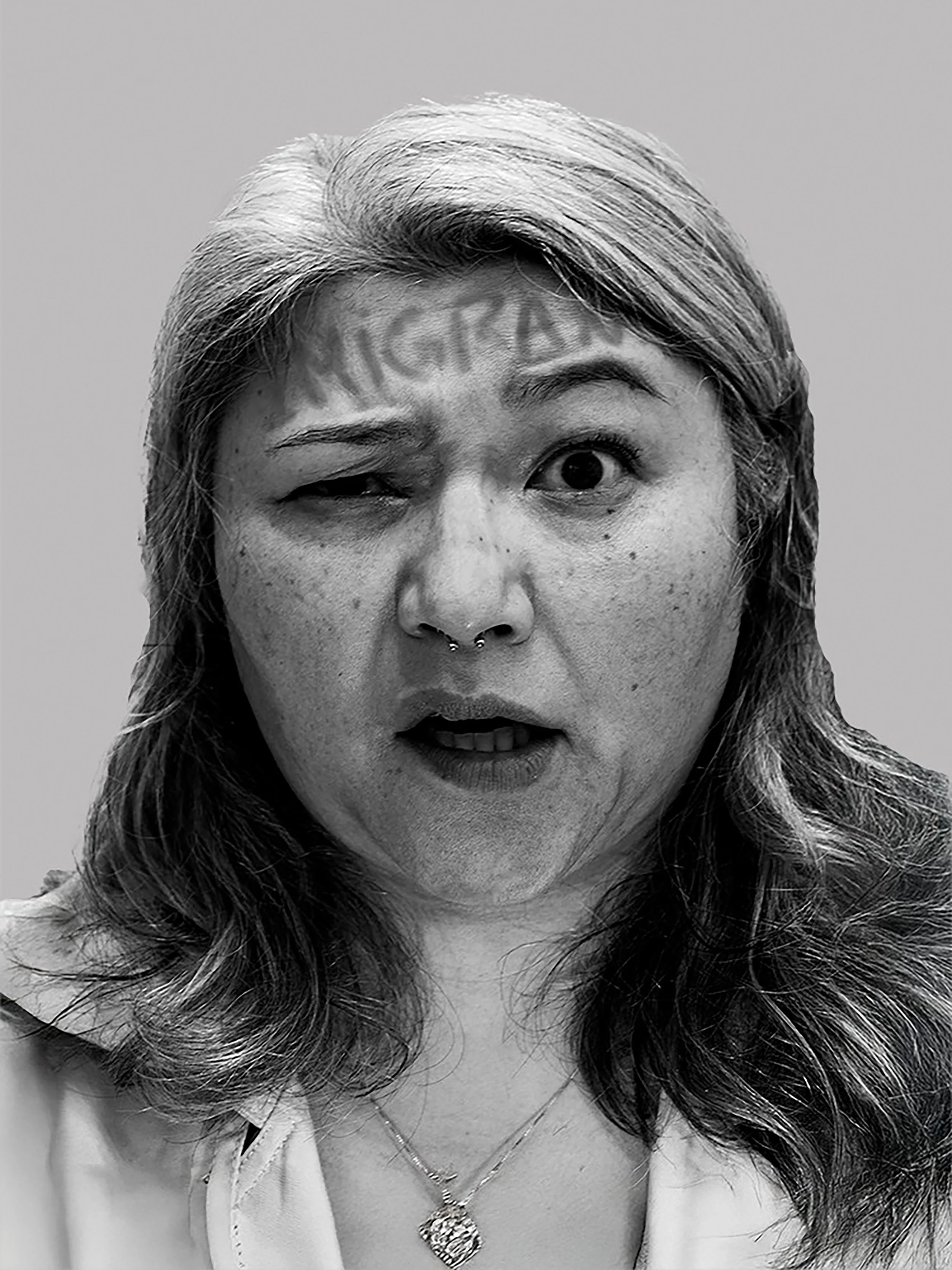 Fotografia em preto e branco selecionada para a exposição coletiva Invisibilidades, mostrando um retrato feminino com a palavra "IMIGRANTE" escrita na testa.