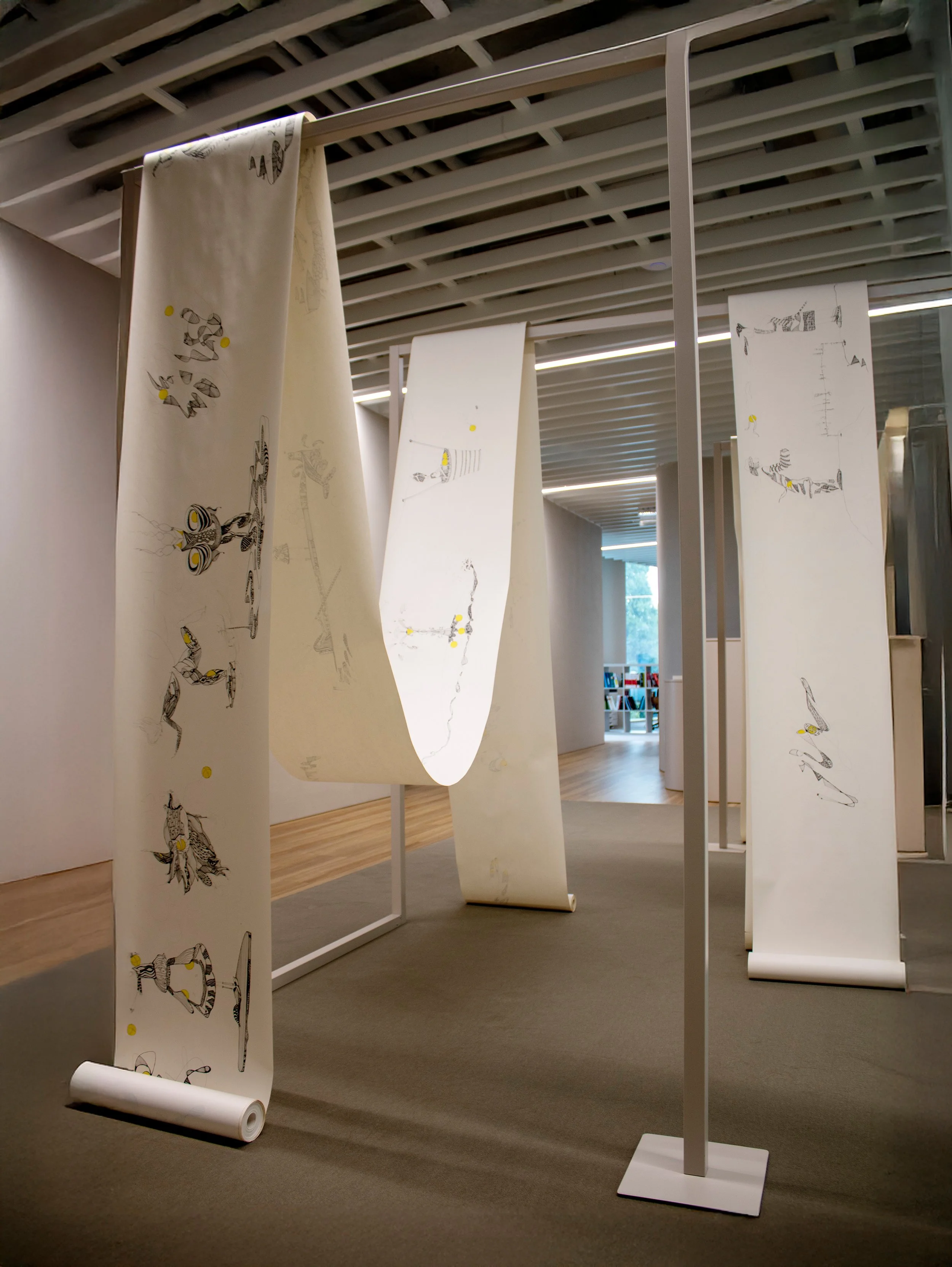 Vista da exposição Humanas Conexões, de Sandra Unglert Fernandes, mostrando três dos quatro rolos contínuos de desenho suspensos no espaço expositivo.