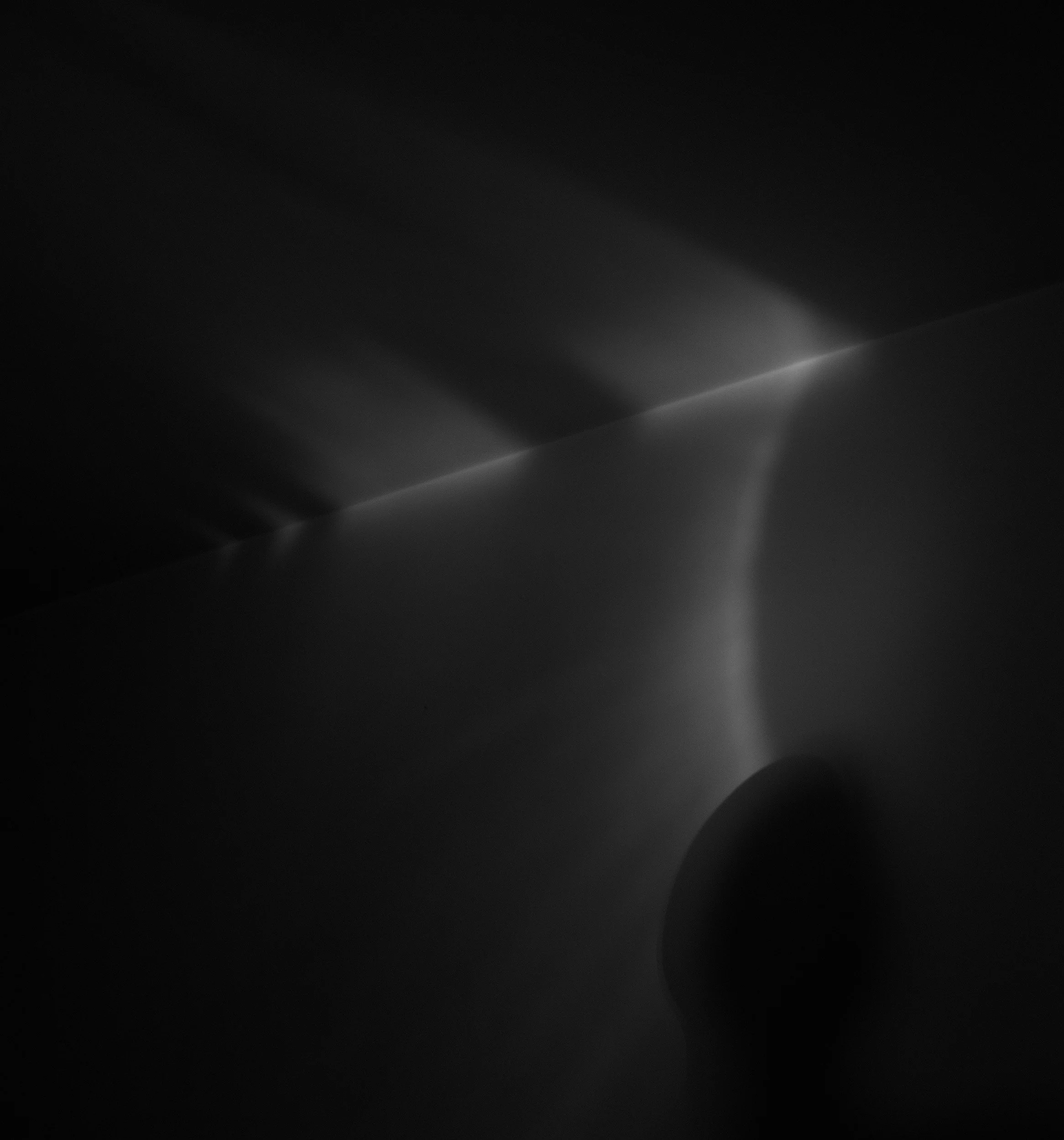 Fotografia digital em preto e branco, integrante da Série Digital 2, de Sandra Unglert Fernandes, mostrando reflexos luminosos sobre uma parede e a silhueta de uma figura humana.