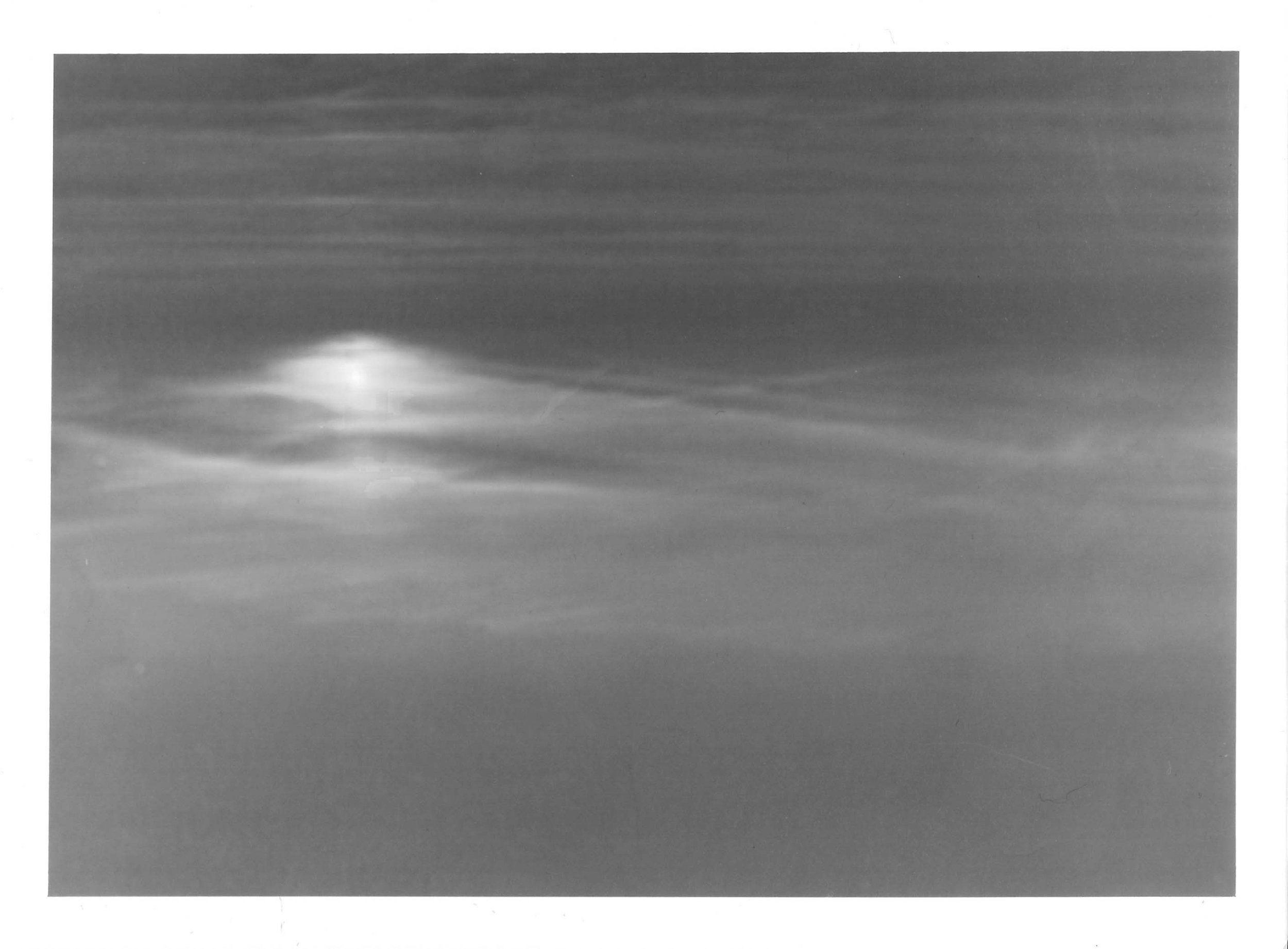 Fotografia analógica em preto e branco, integrante da Série 3, de Sandra Unglert Fernandes, apresentando foco de luz difuso sobre uma superfície, com camadas suaves de tons que evocam uma aquarela.