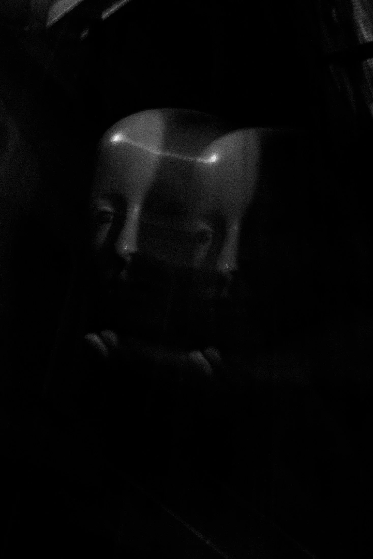 Fotografia digital em preto e branco, integrante da Série Digital 1, de Sandra Unglert Fernandes, mostrando dois rostos parcialmente sobrepostos e iluminados sobre fundo escuro.