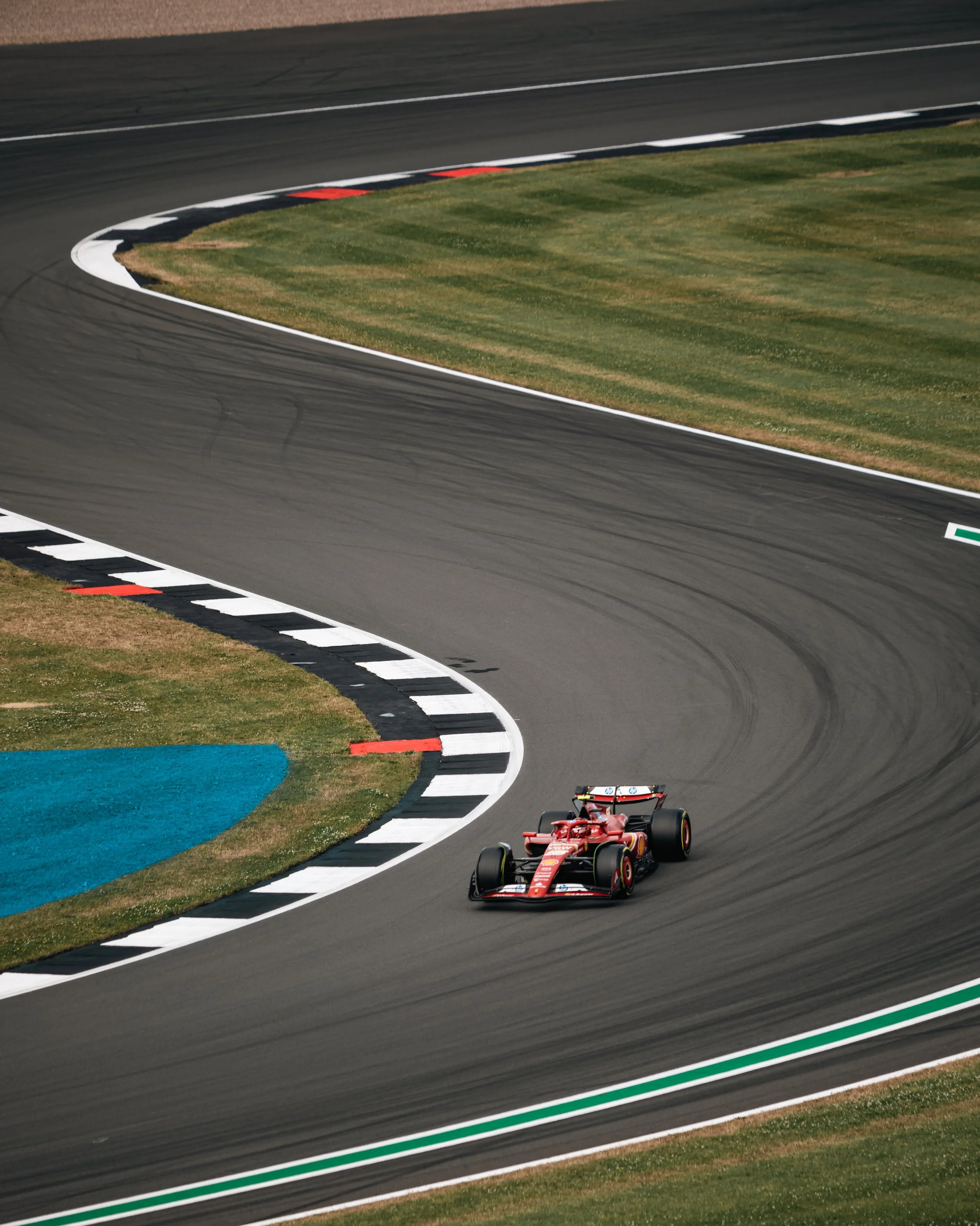 A red Formula 1 race car speeding on a racetrack with curving turn, surrounded by green grass and painted curbs.