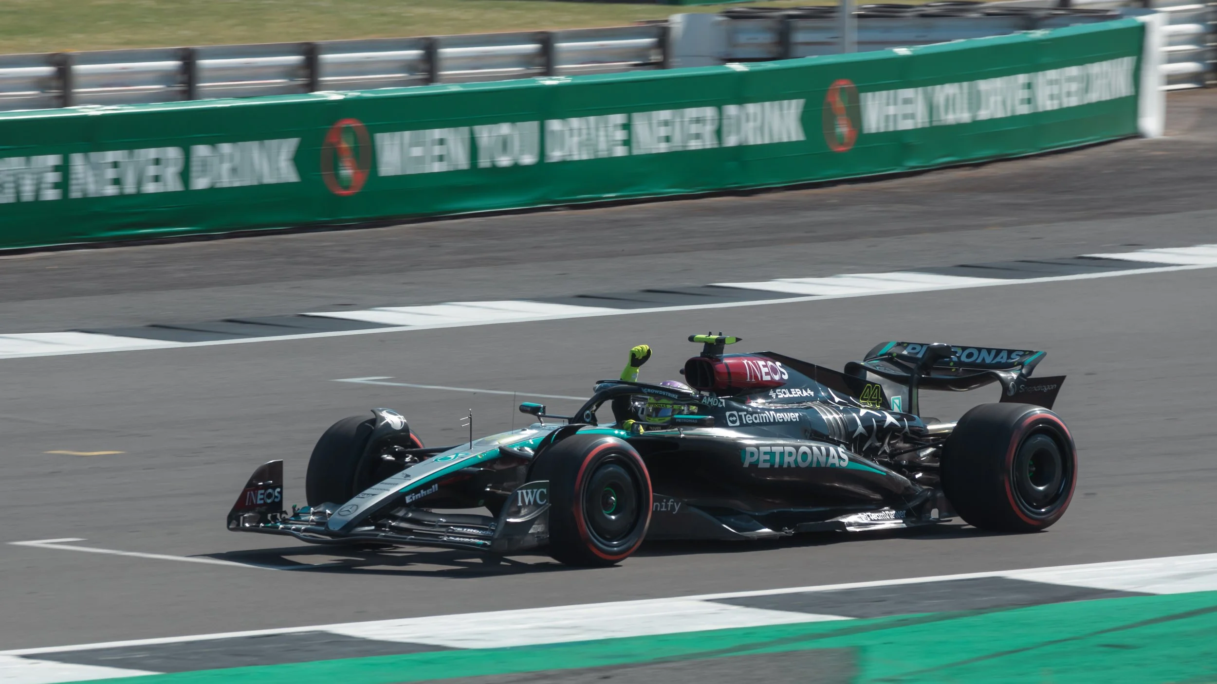 A Formula 1 race car speeding on a race track, with green barriers and advertisement banners in the background.