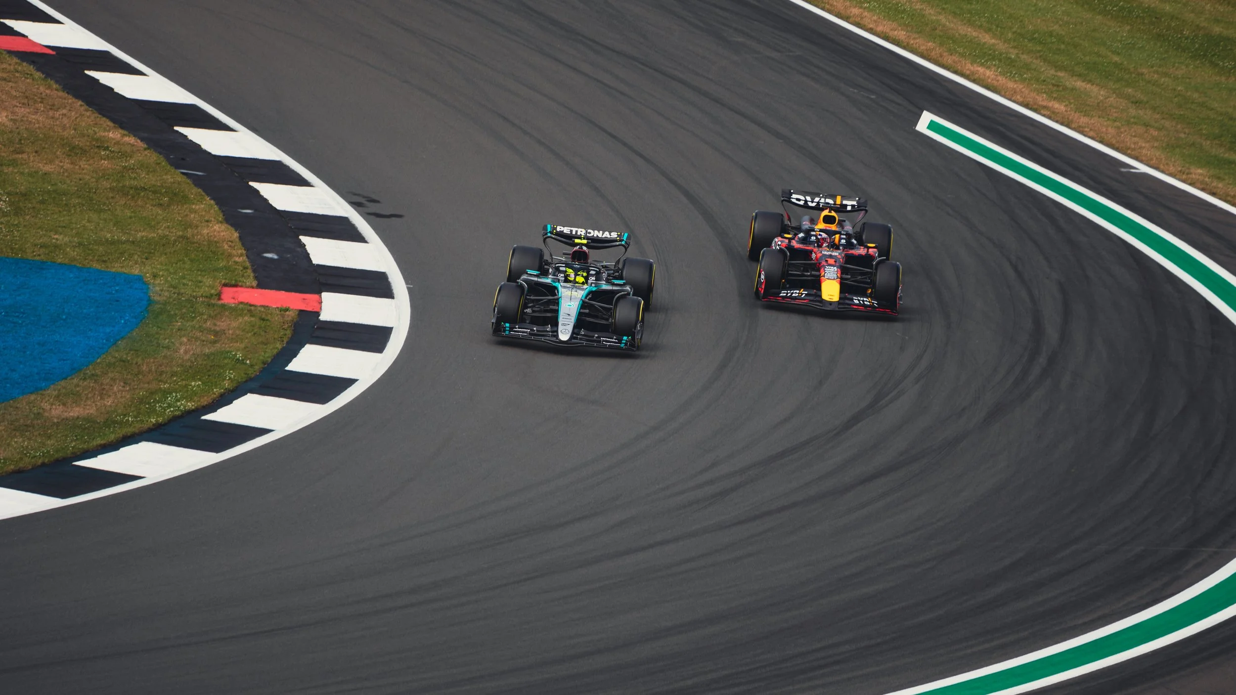 Two race cars on a racetrack, one Mercedes and one Red Bull, racing through a curve during a motorsport event.