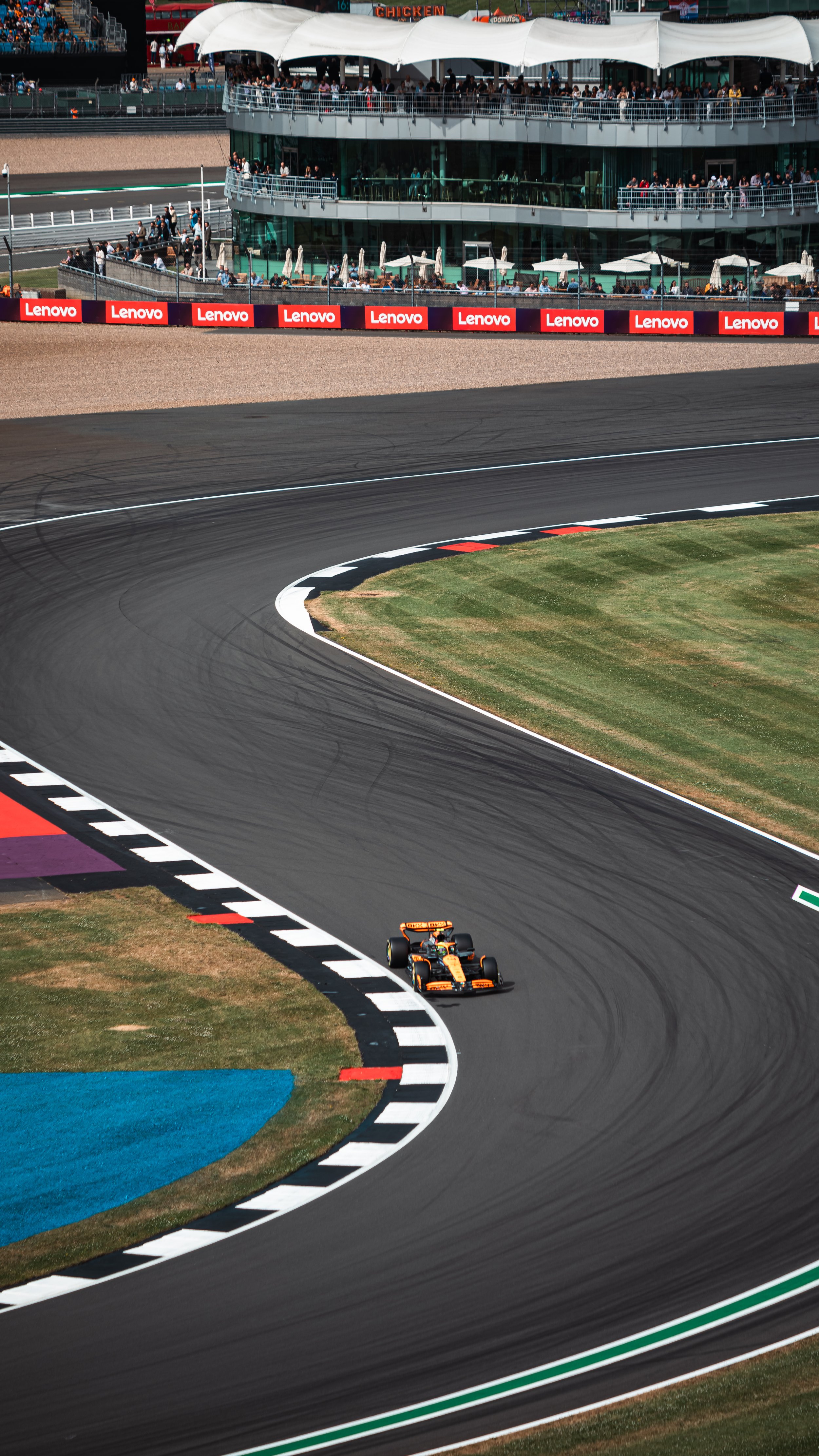 A racing car on a race track with spectators and buildings in the background.