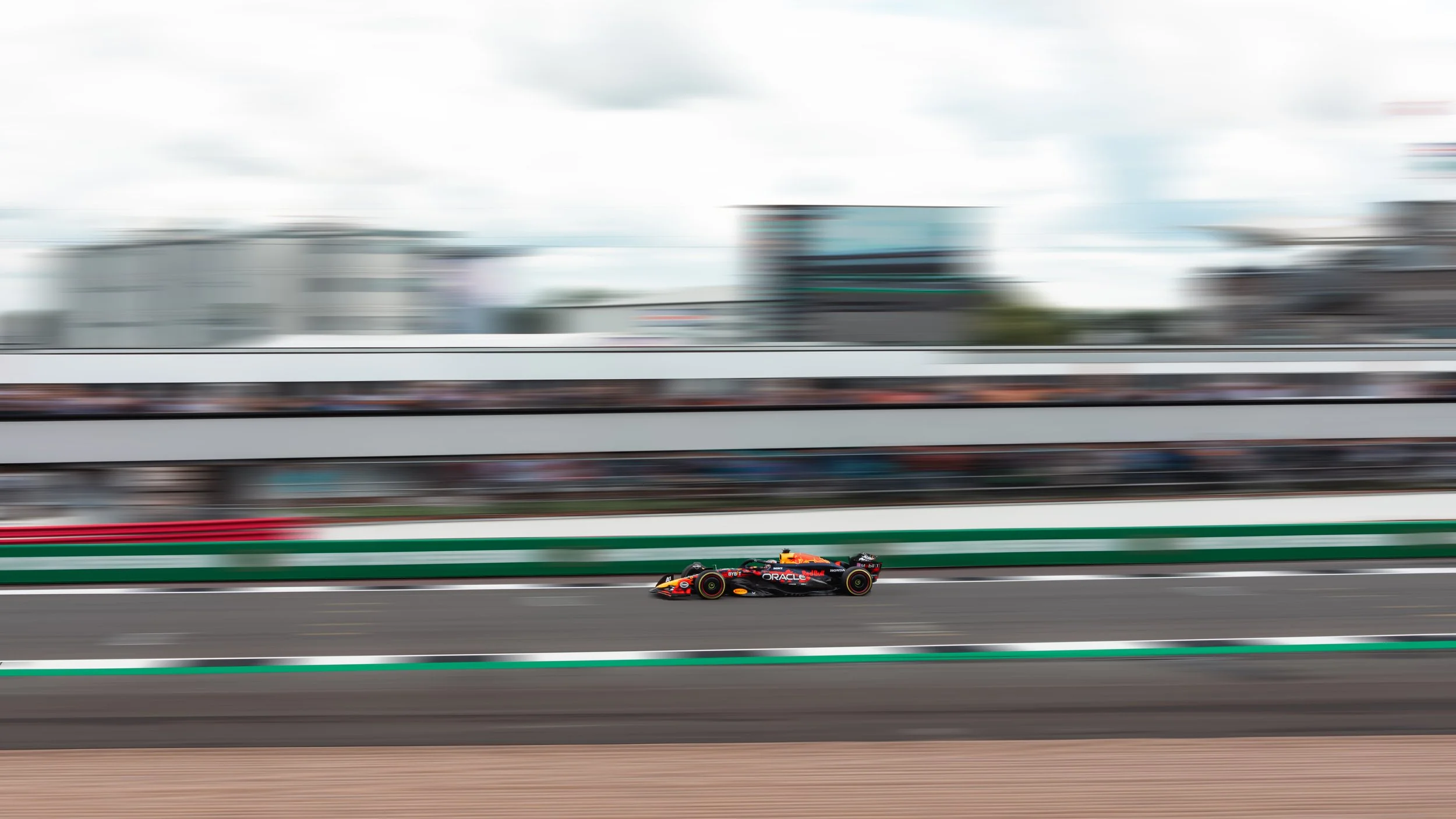 A Formula 1 race car speeding on a race track with blurred background of buildings and spectators.